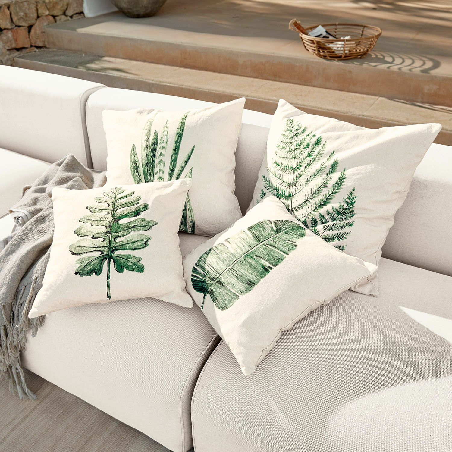 Lot de 4 housses de coussins Marly Ensemble de quatre coussins crème avec imprimés de feuilles vertes sur un canapé clair, décoration intérieure
