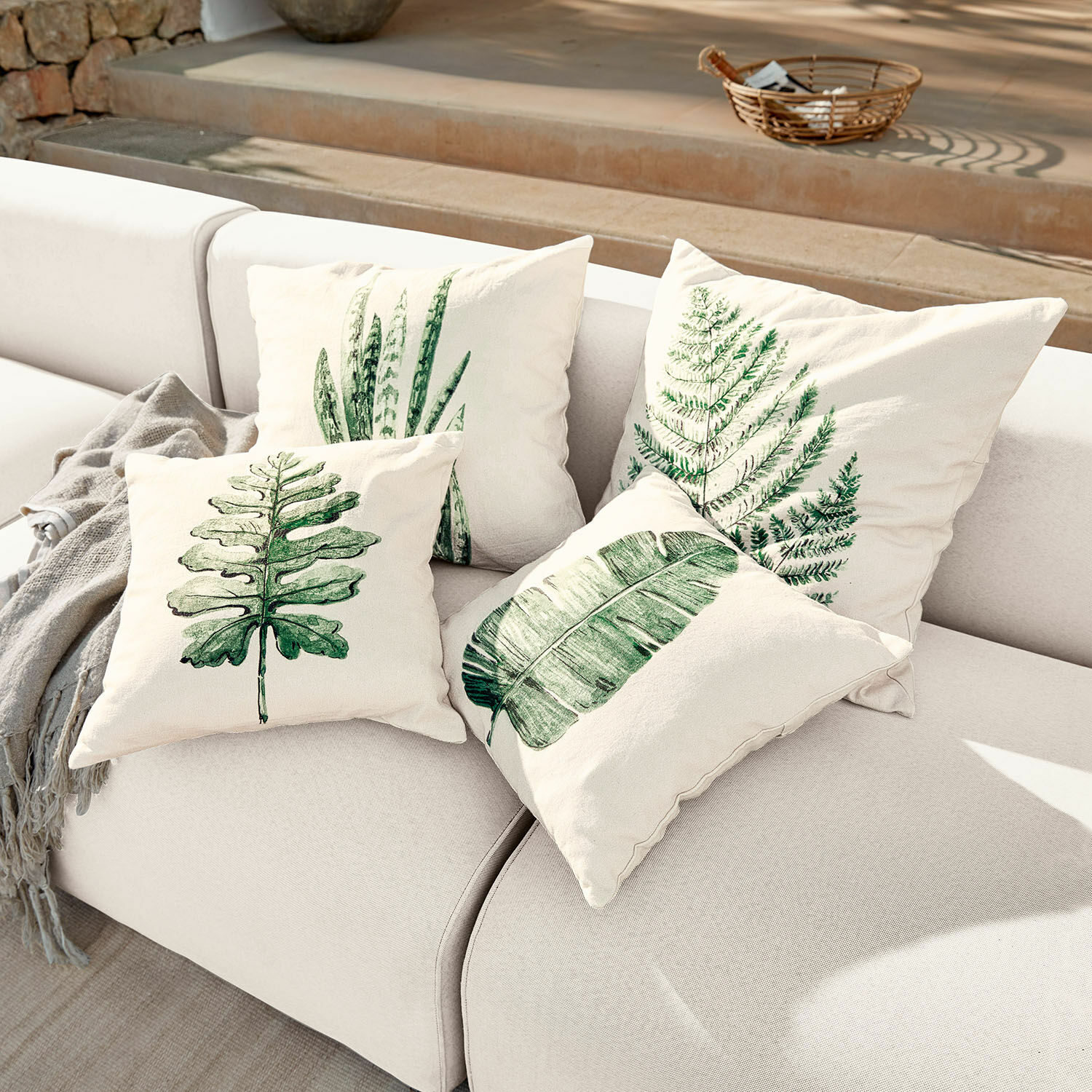 Lot de 4 housses de coussins Marly Ensemble de quatre coussins crème avec imprimés de feuilles vertes sur un canapé clair, décoration intérieure