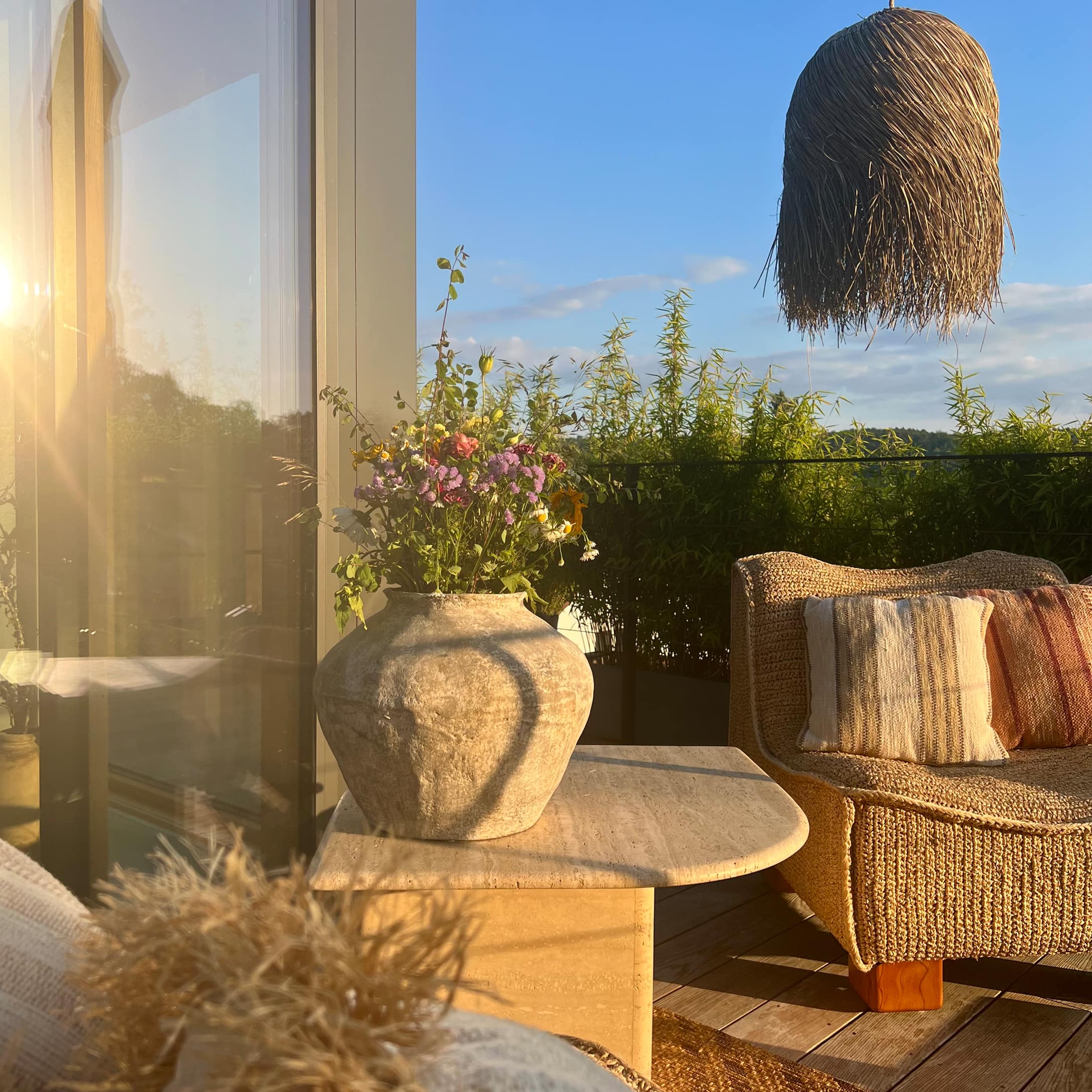 Grand vase en céramique avec fleurs sur table en pierre sur terrasse avec canapé en osier et lampe en herbe marine
