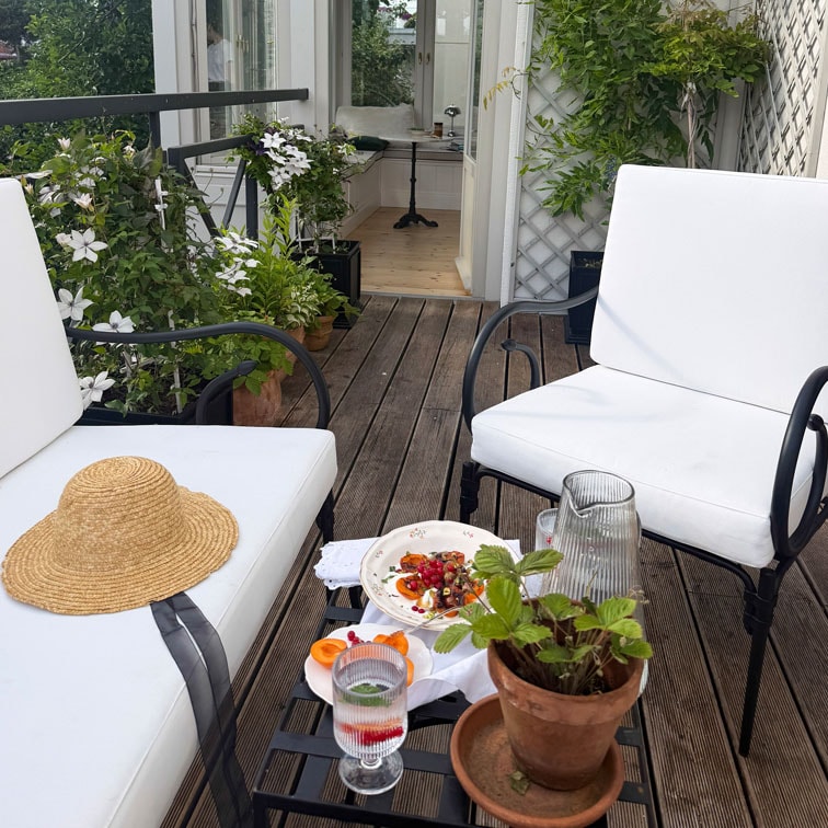 Terrasse avec fauteuils en métal blanc, sol en bois et plantes en pot pour un coin détente extérieur