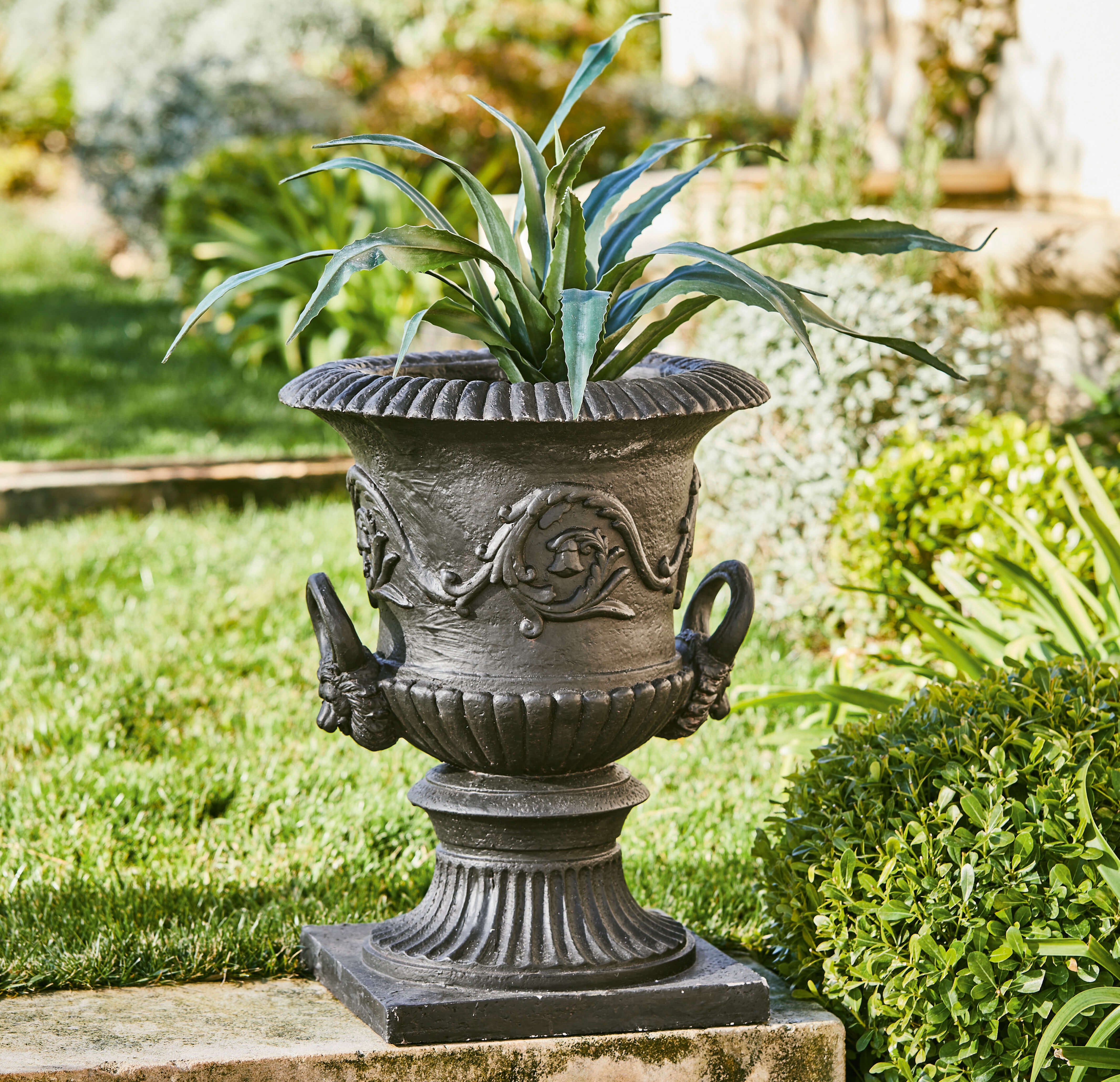 Jardinière noire en fonte avec décor végétal, style classique, placée dans un jardin verdoyant