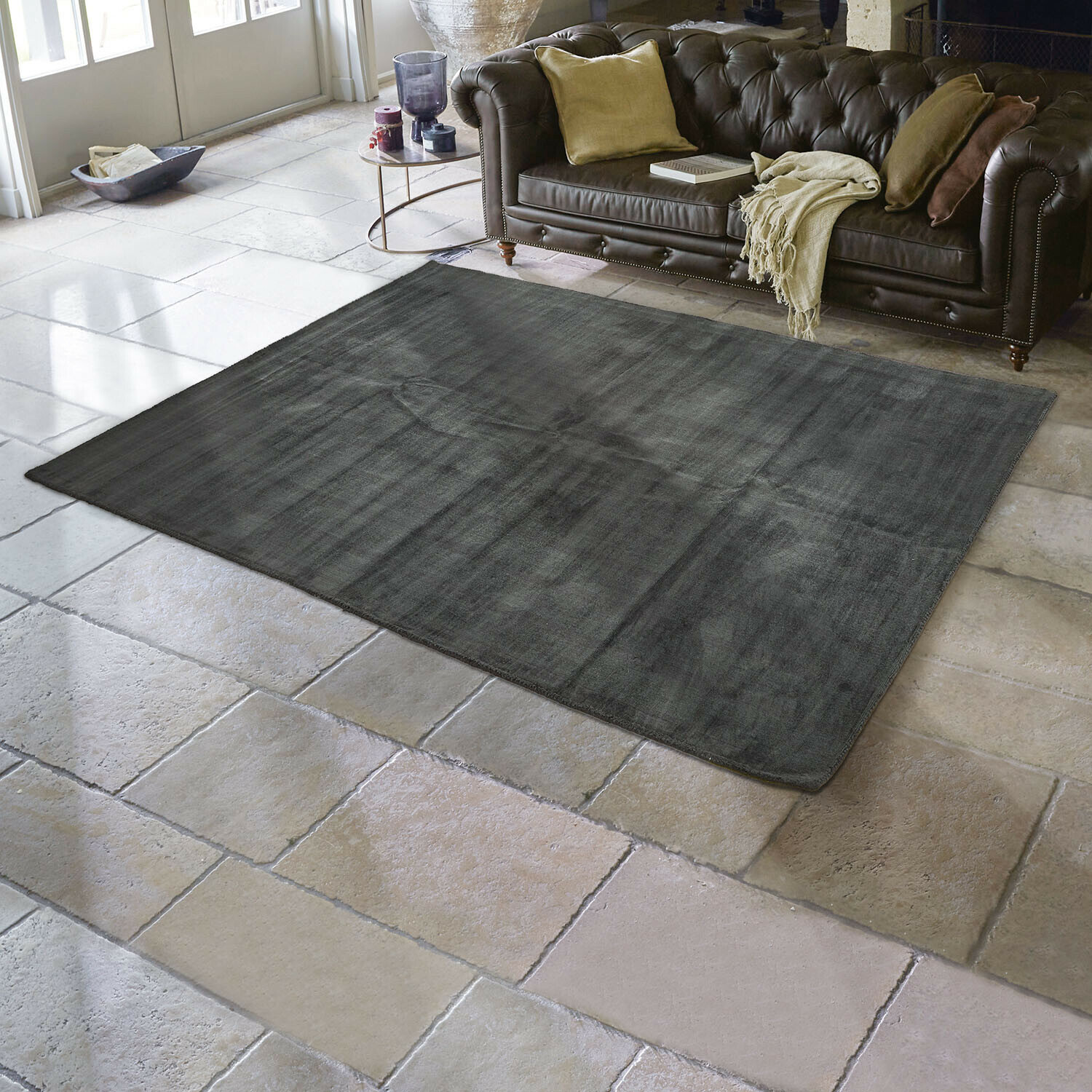 Tapis Mariselle Tapis gris foncé en tissu doux sur sol en pierre claire dans un salon avec canapé en cuir marron