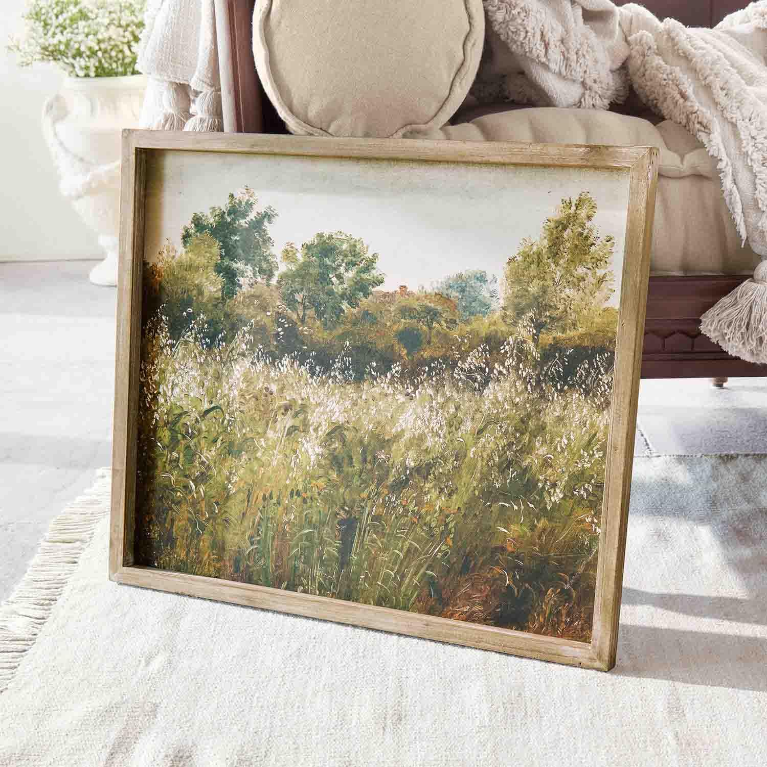 Tableau paysage avec arbres verts et prairie encadré en bois posé sur un tapis clair