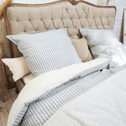 Tête de lit capitonnée beige avec literie rayée grise et couette crème dans une chambre cosy