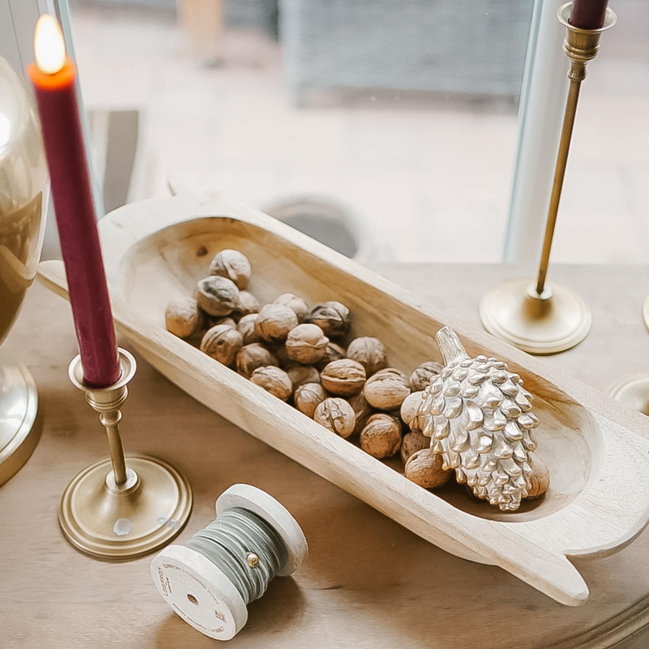 Bol en bois avec des noix et une décoration pomme de pin dorée sur une table de Noël avec bougies rouges