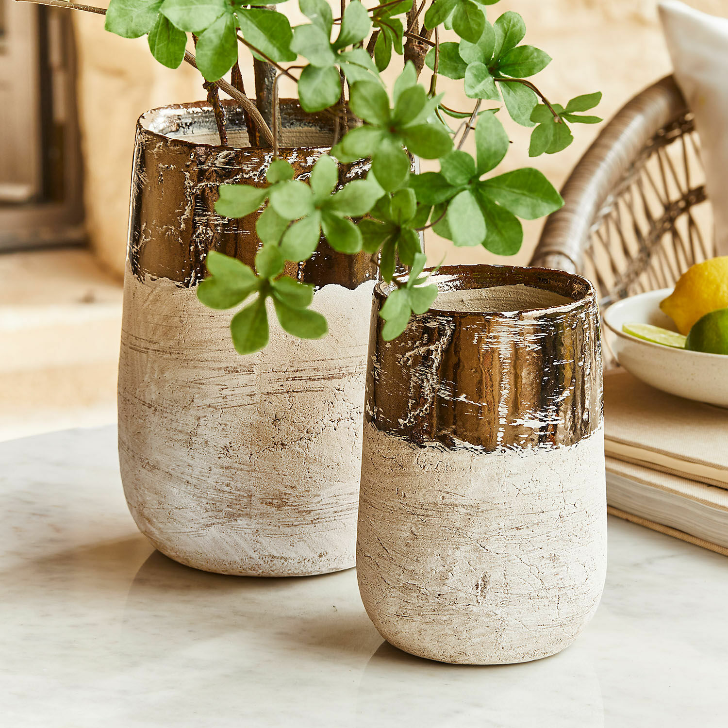 Lot de 2 vases Hafira Deux vases en céramique beige et marron sur une table en marbre avec des feuilles vertes