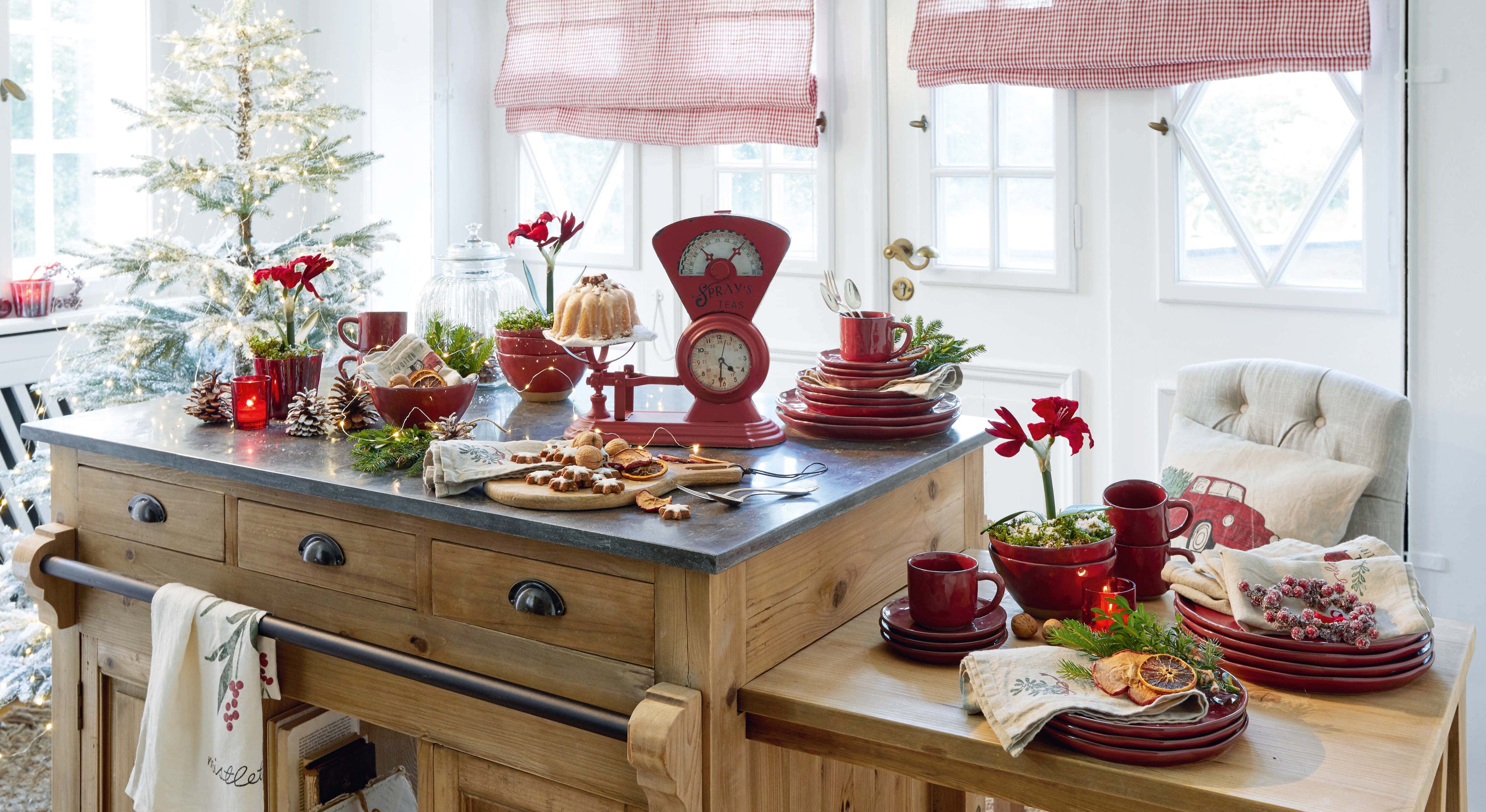Cuisine avec îlot en bois, vaisselle rouge en céramique et décoration de Noël avec guirlandes lumineuses LED