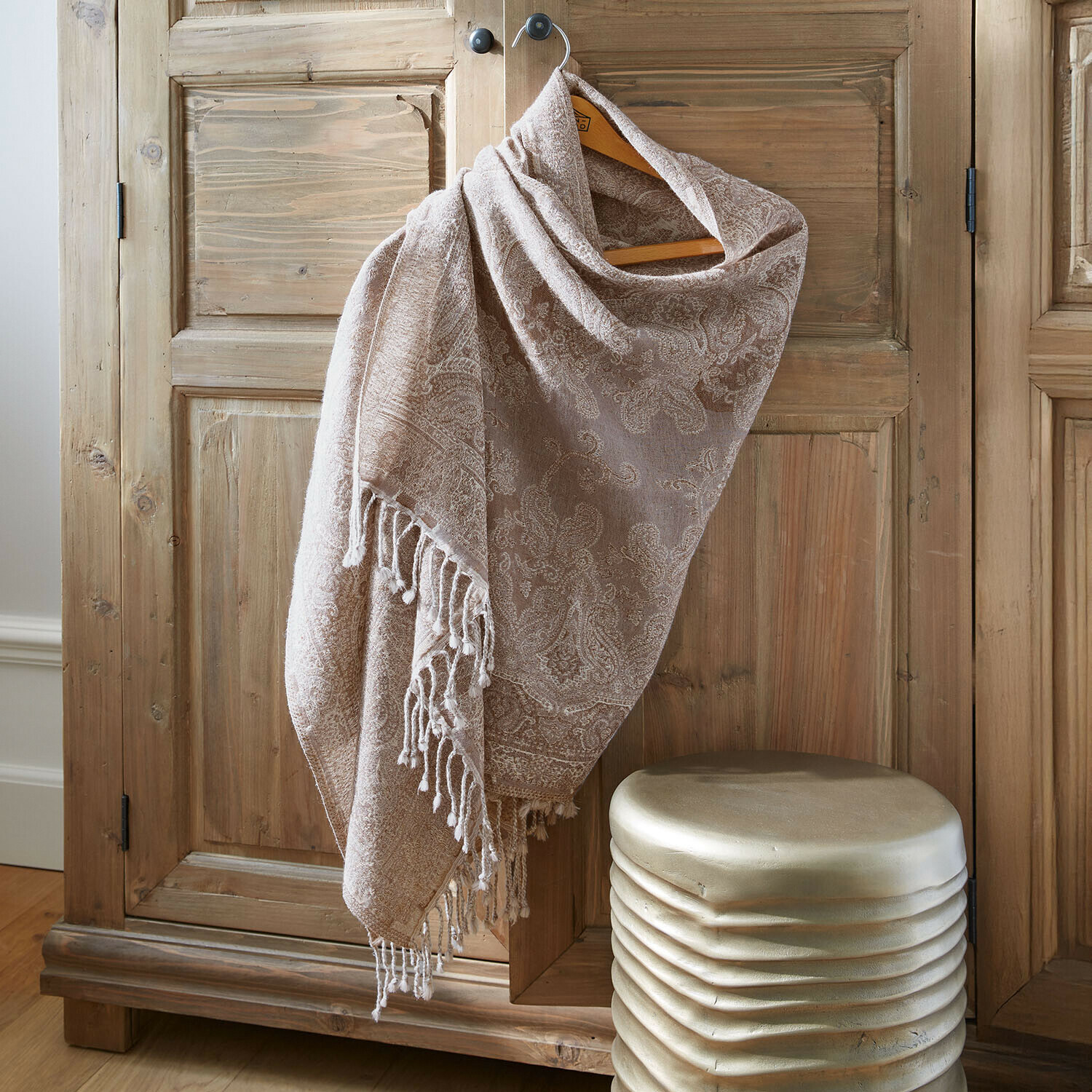 Écharpe beige à motif cachemire avec franges suspendue sur une armoire en bois, tissu doux et décoratif