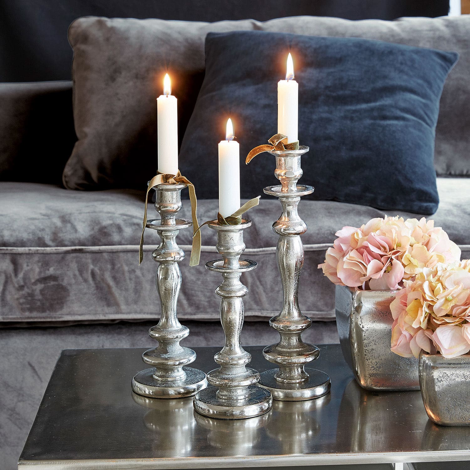 Lot de 3 bougeoirs Borga Ensemble de trois chandeliers en métal argenté avec bougies blanches sur une table basse dans un salon
