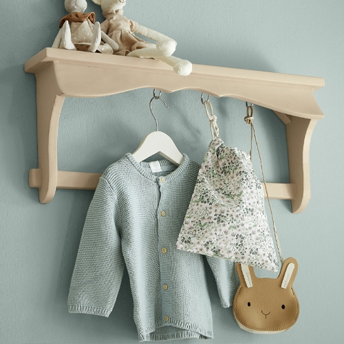 Étagère murale beige en bois avec crochets, portant un pull bleu clair et un sac à motif floral