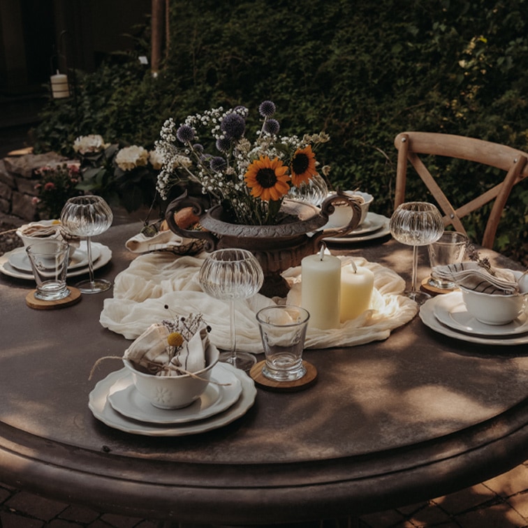 Table ronde de jardin décorée avec bougies et fleurs dans un vase en métal pour une réception extérieure.