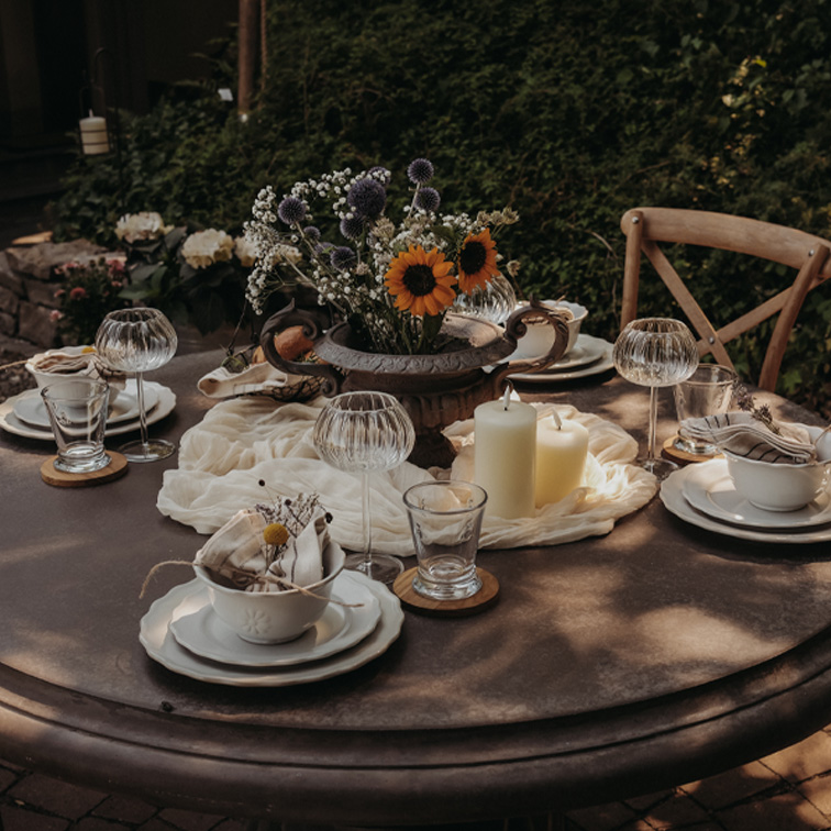 Table ronde de jardin décorée avec bougies et fleurs dans un vase en métal pour une réception extérieure.