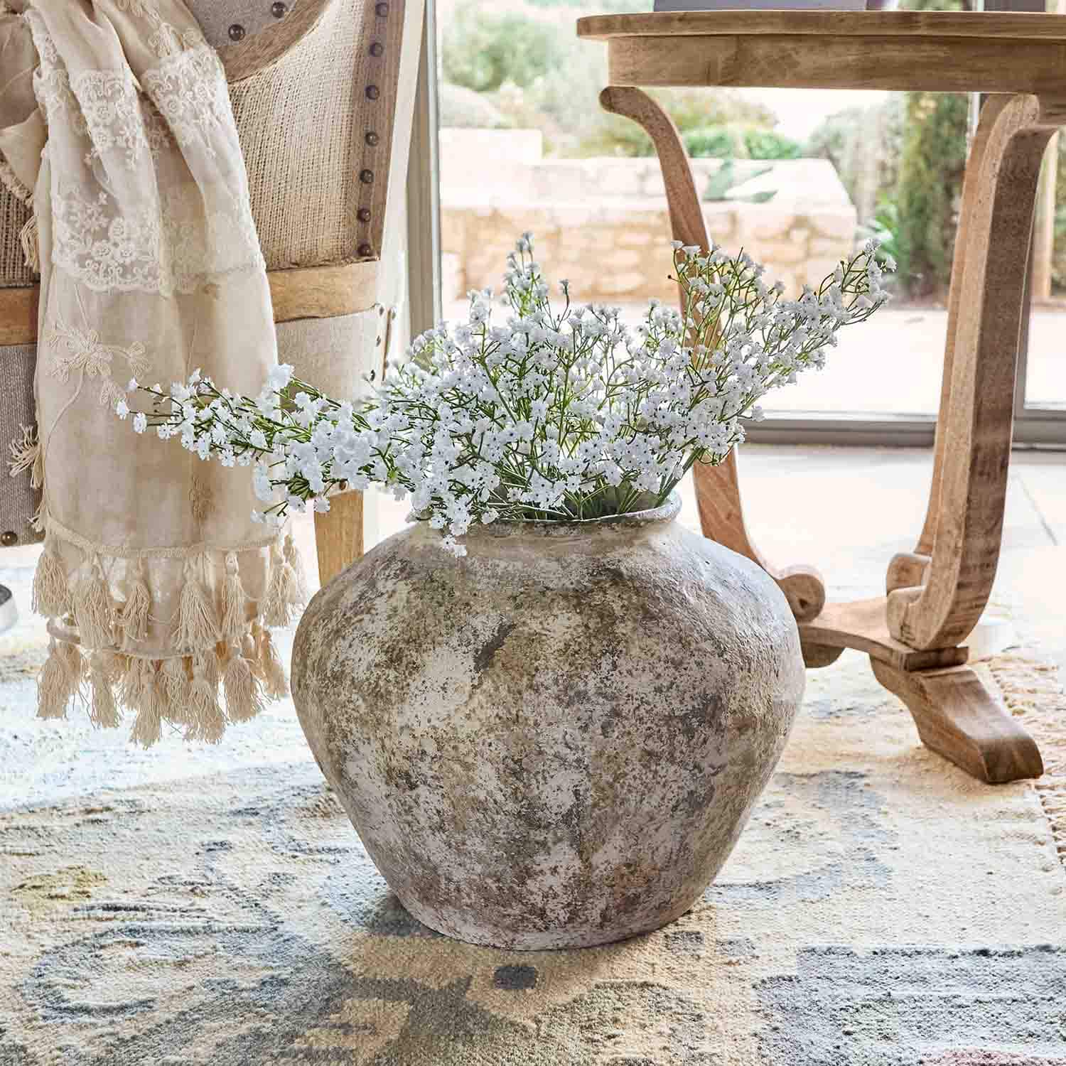 Grand vase en céramique couleur naturelle avec fleurs blanches sur tapis dans un intérieur lumineux