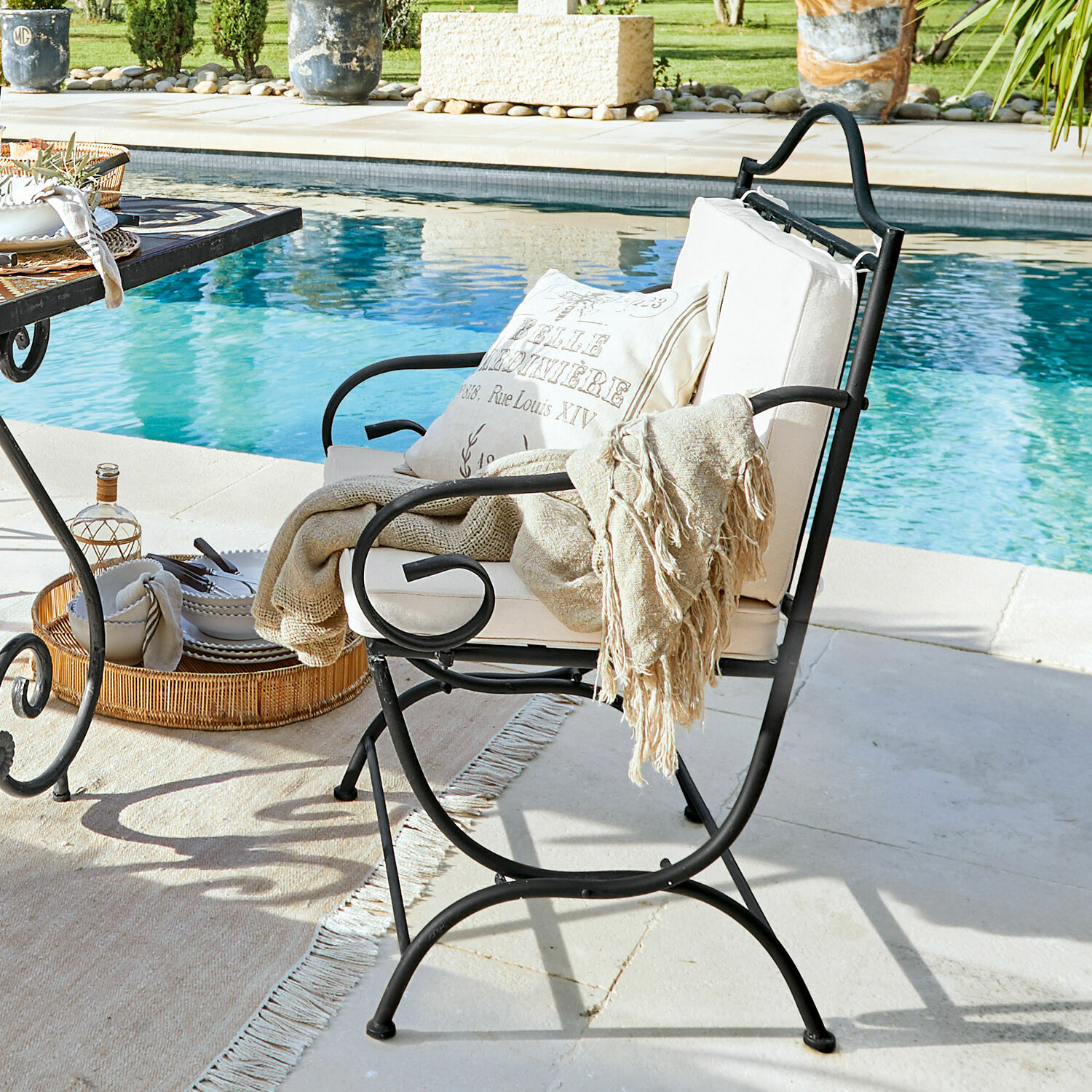 Chaise Avanton Fauteuil de jardin en métal noir avec coussin crème et plaid beige au bord de la piscine, mobilier extérieur