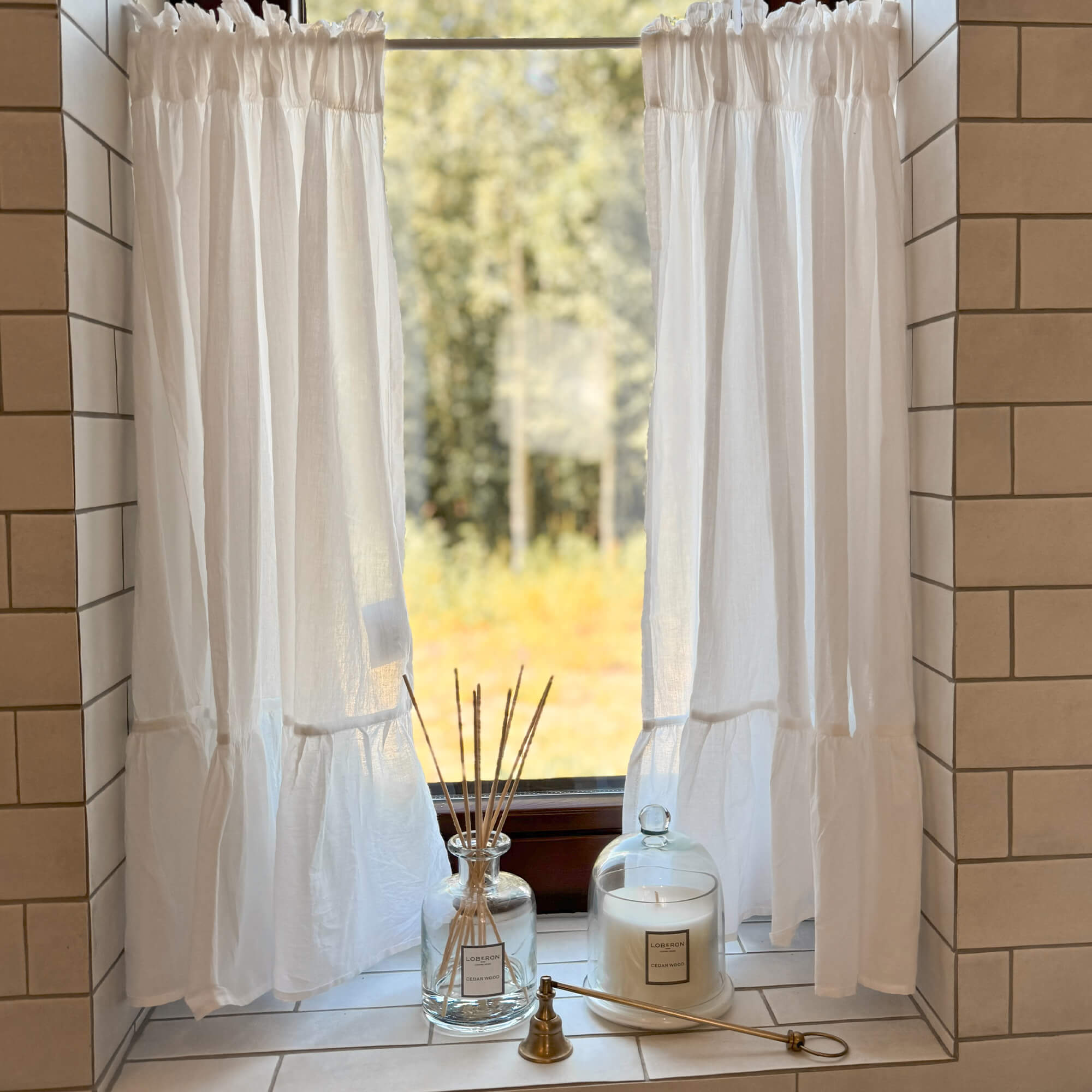 Rideaux blancs en lin sur une fenêtre avec bougie décorative et diffuseur parfumé sur le rebord