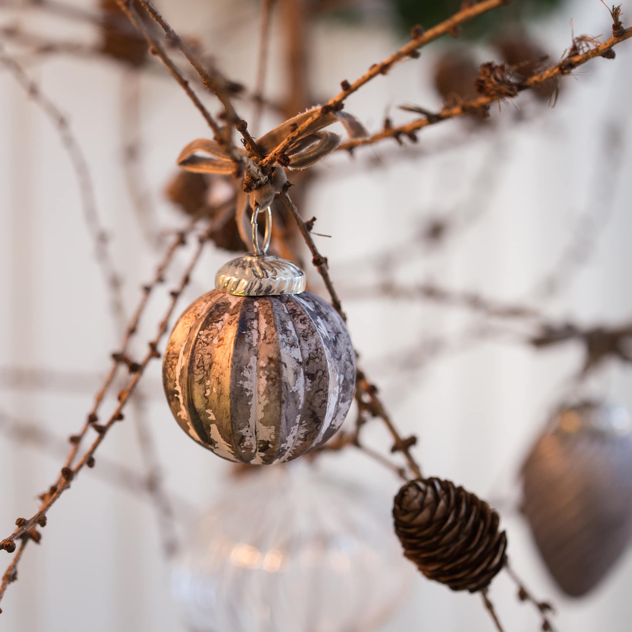 Boule de Noël en verre argenté et brun suspendue à une branche avec une pomme de pin, décoration festive