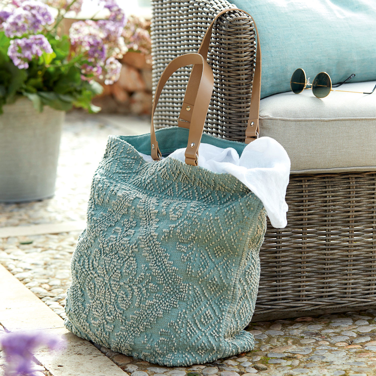 Cabas Vicel Sac turquoise en tissu texturé avec poignées marron posé près d'un fauteuil en osier et lunettes de soleil