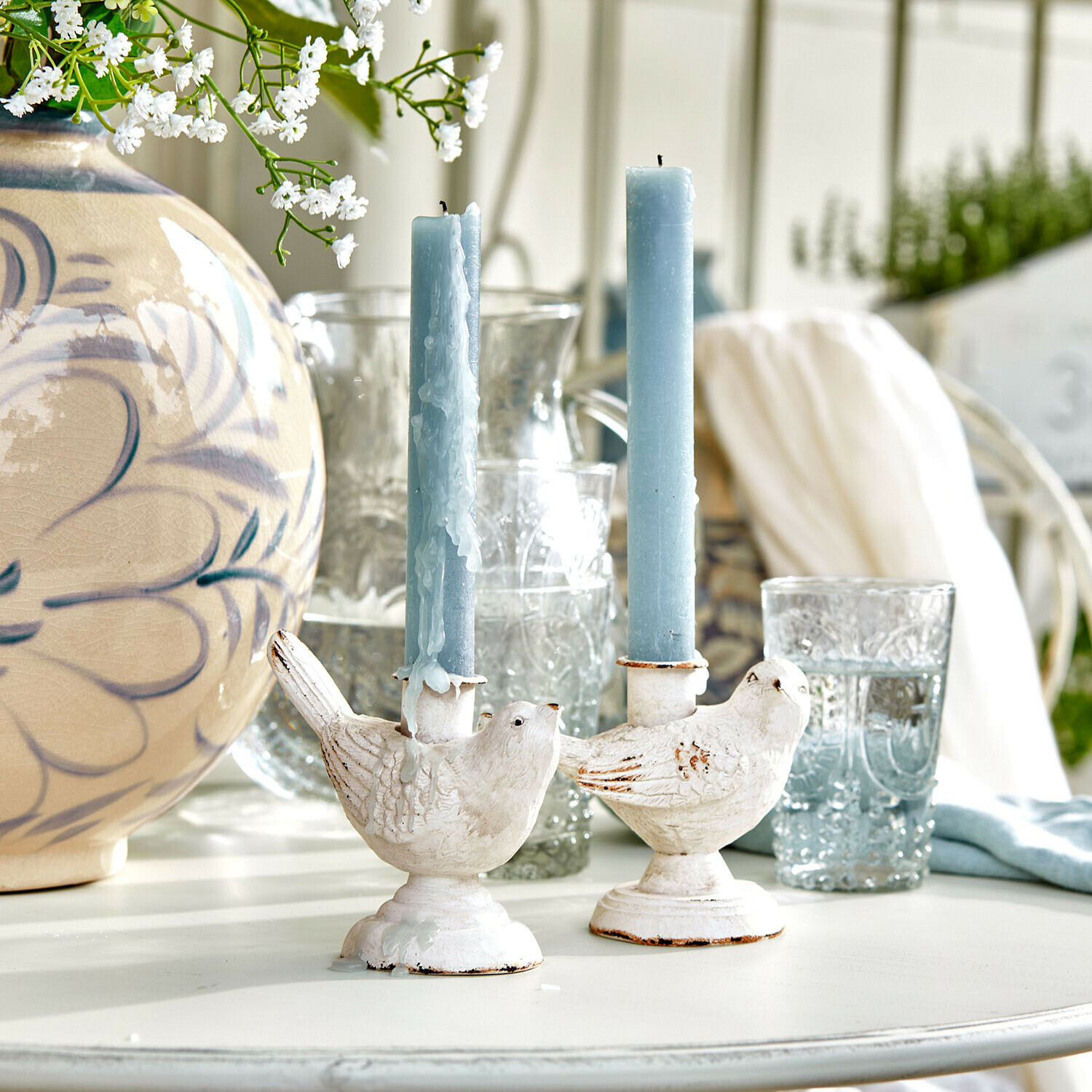 Lot de 2 bougeoirs Finna Bougeoirs blancs en forme d'oiseaux avec bougies bleues sur une table claire décorée de fleurs