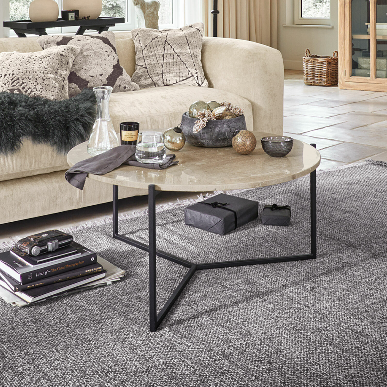 Table basse Émorieux Table basse ronde avec plateau en marbre beige et pieds en métal noir sur tapis gris dans un salon