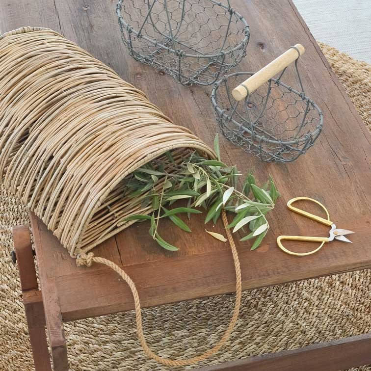 Panier en osier avec poignée en corde sur table en bois avec branches vertes et ciseaux de jardinage dorés