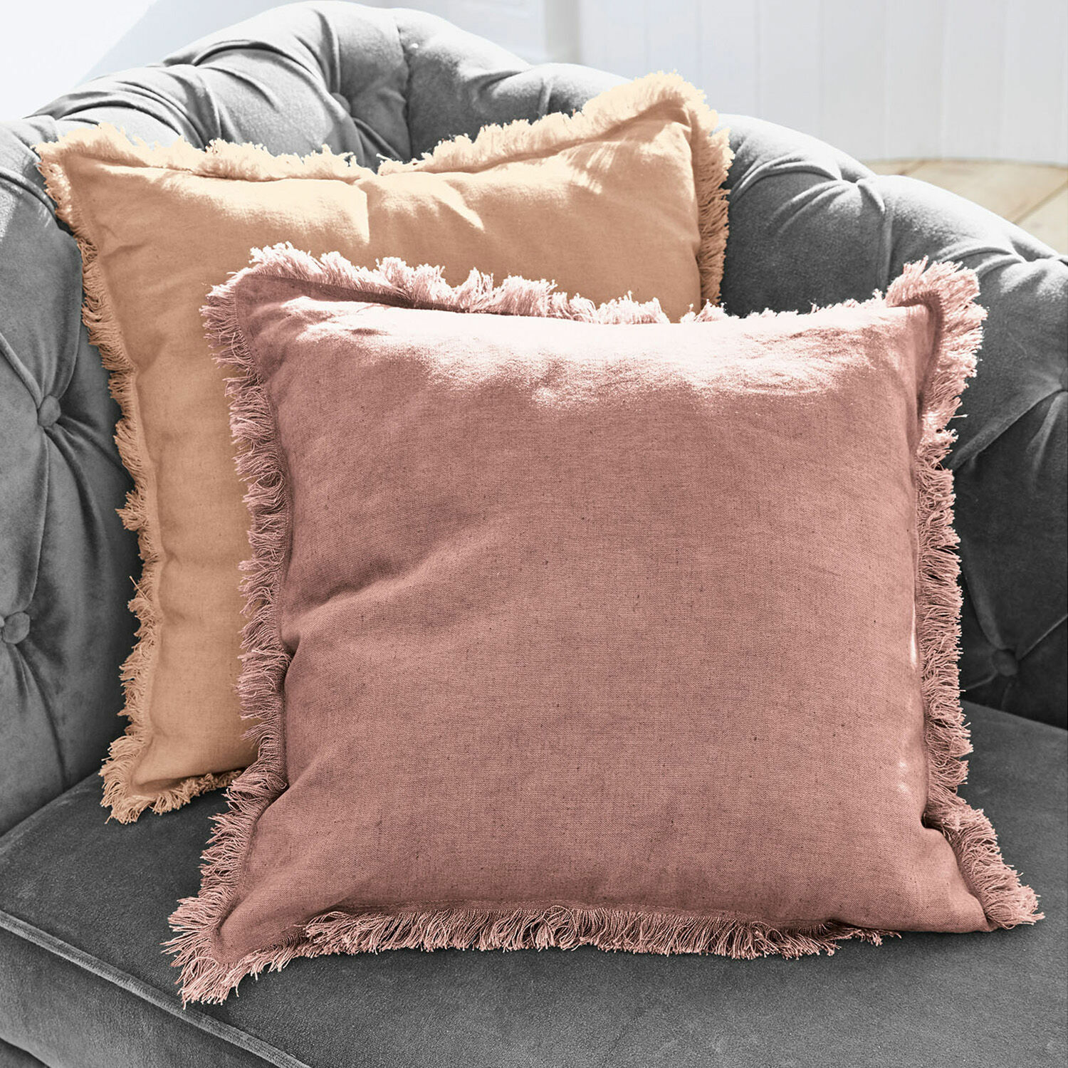 Lot de 2 housses de coussins Quebo Ensemble de deux coussins décoratifs en lin avec franges rose et beige sur un canapé gris