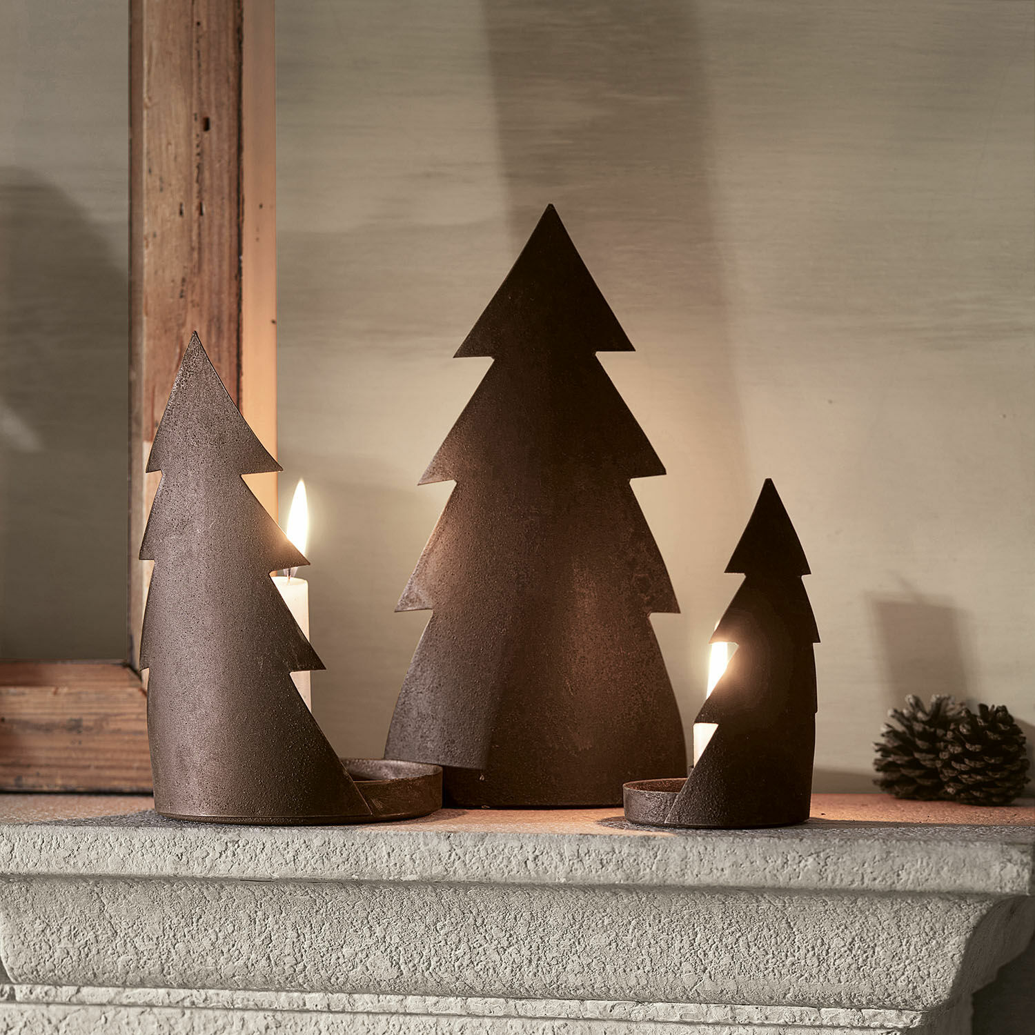 Lot de 3 bougeoirs Ageville Ensemble de trois bougeoirs en métal rouillé en forme de sapins sur une cheminée, décoration de Noël