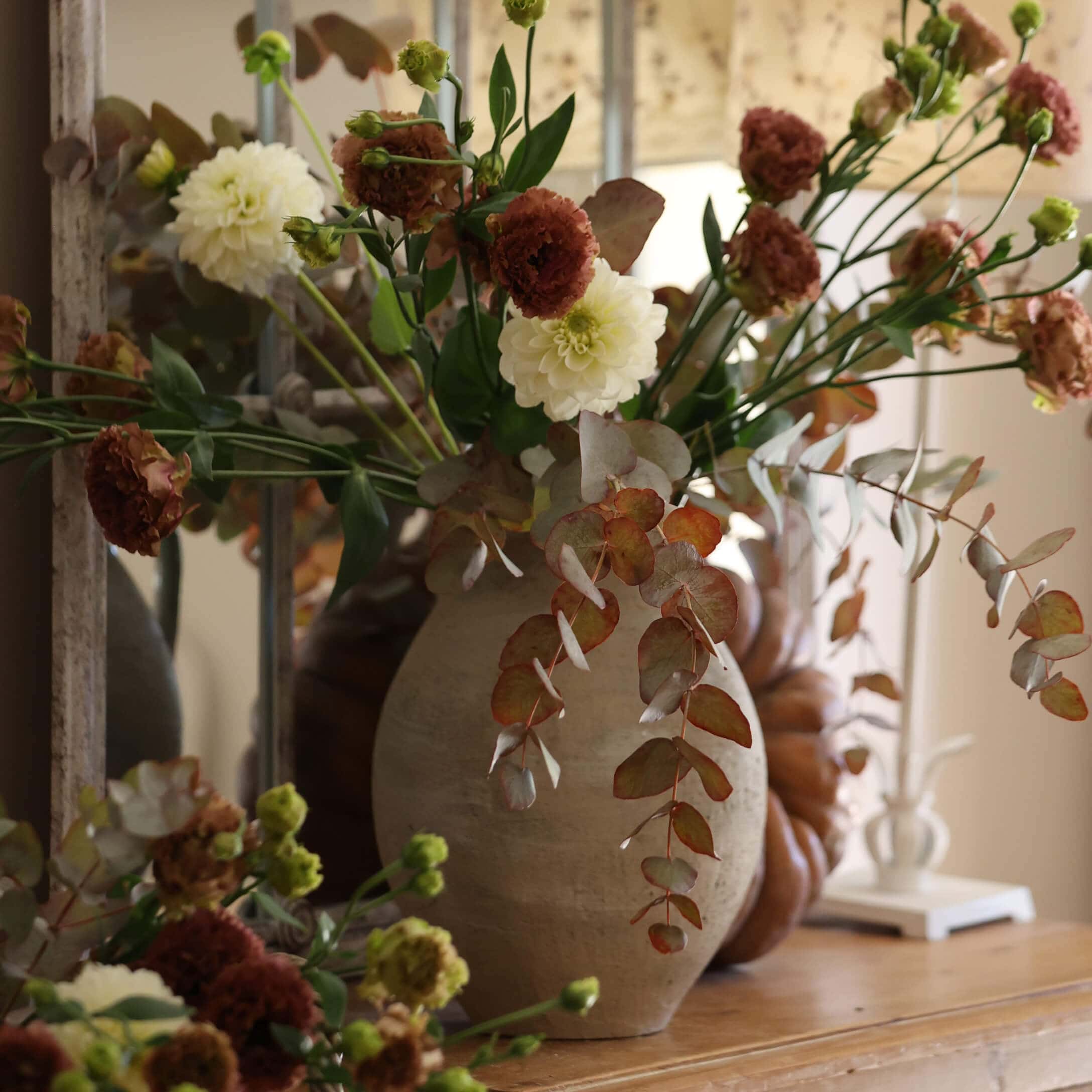 Vase en céramique beige avec bouquet de fleurs blanches et brunes sur une table en bois décorative