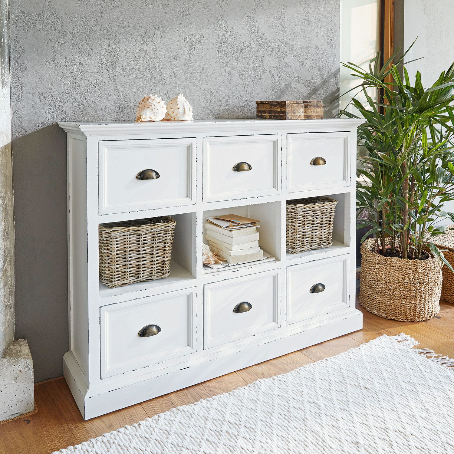 Commode Remilly Commode blanche en bois avec six tiroirs et trois étagères ouvertes, décorations et plante à côté