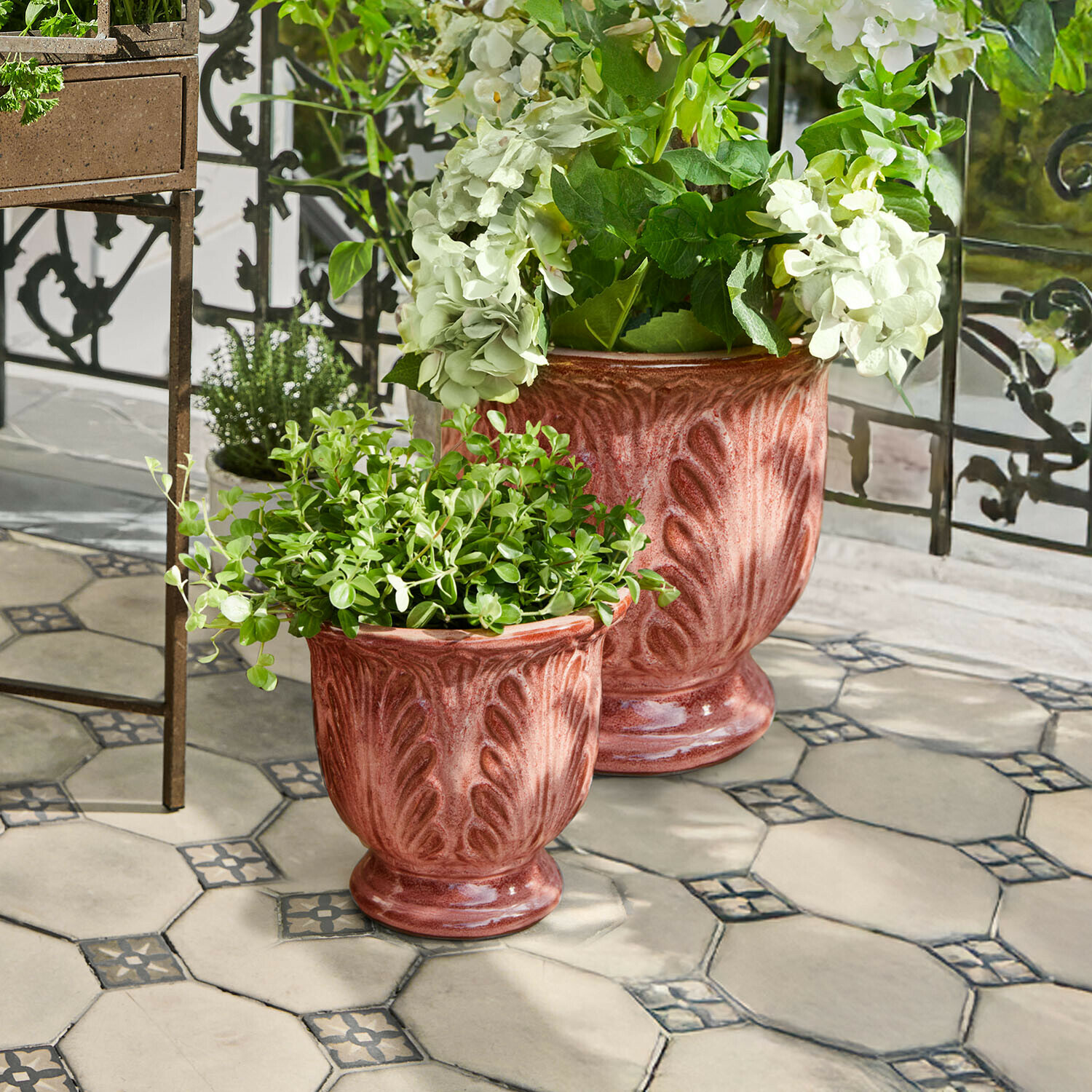 Lot de 2 cache-pots Aurezia Deux pots en céramique couleur rouille avec plantes sur terrasse carrelée et balustrade en métal décoratif