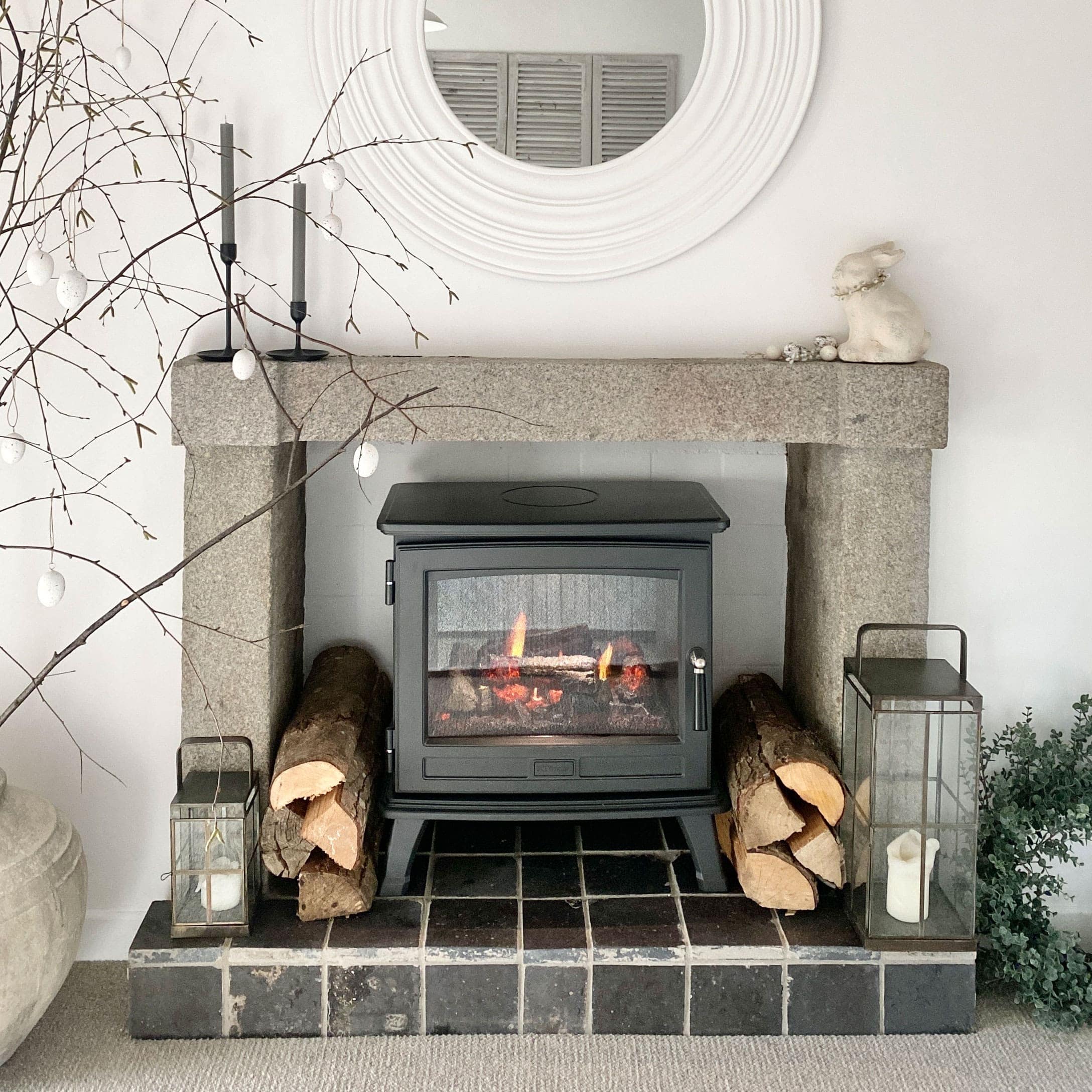 Poêle à bois noir dans une cheminée en pierre avec bûches décoratives et lanternes rustiques