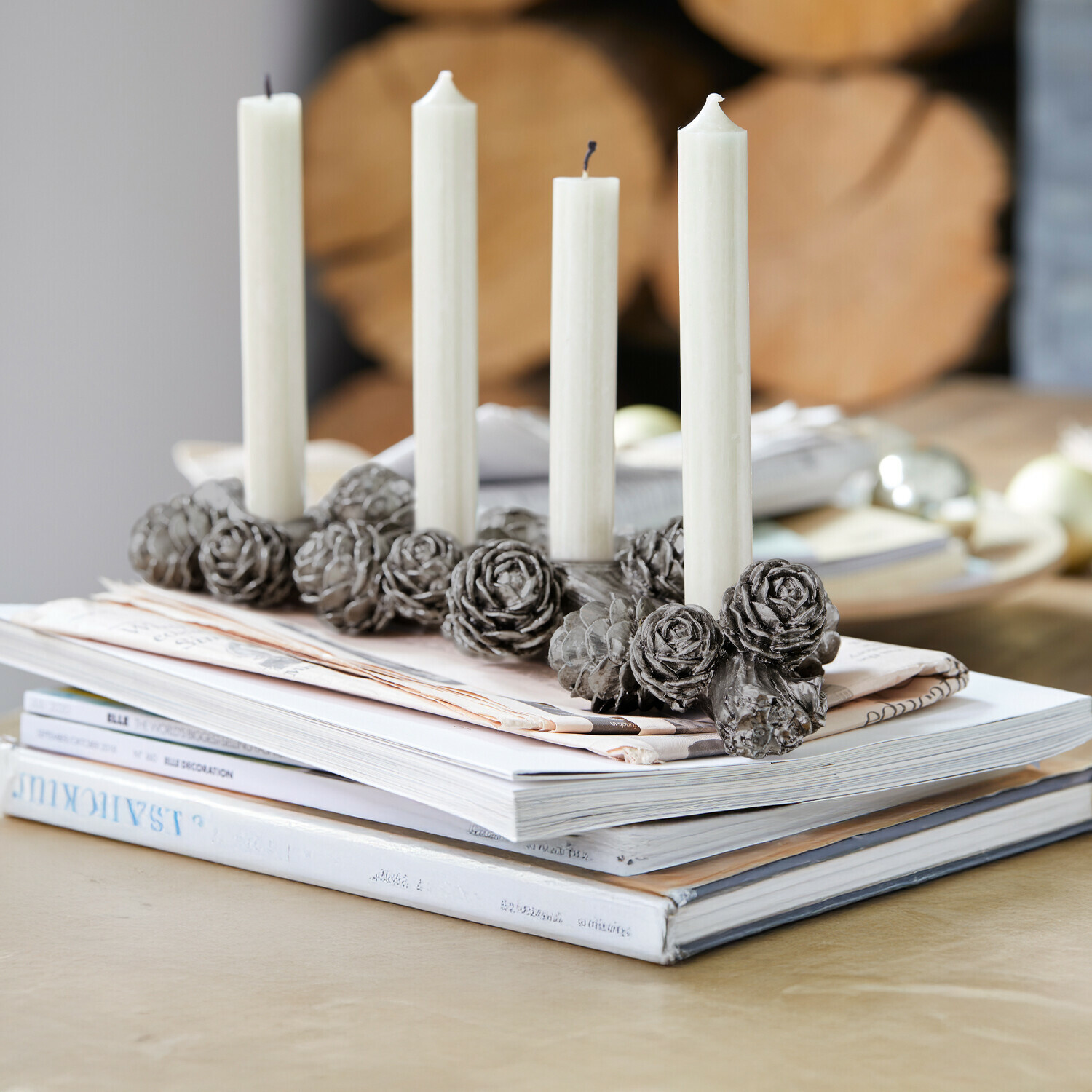 Bougeoir Arasta Bougeoir décoratif gris en forme de pommes de pin avec quatre bougies blanches posé sur des magazines