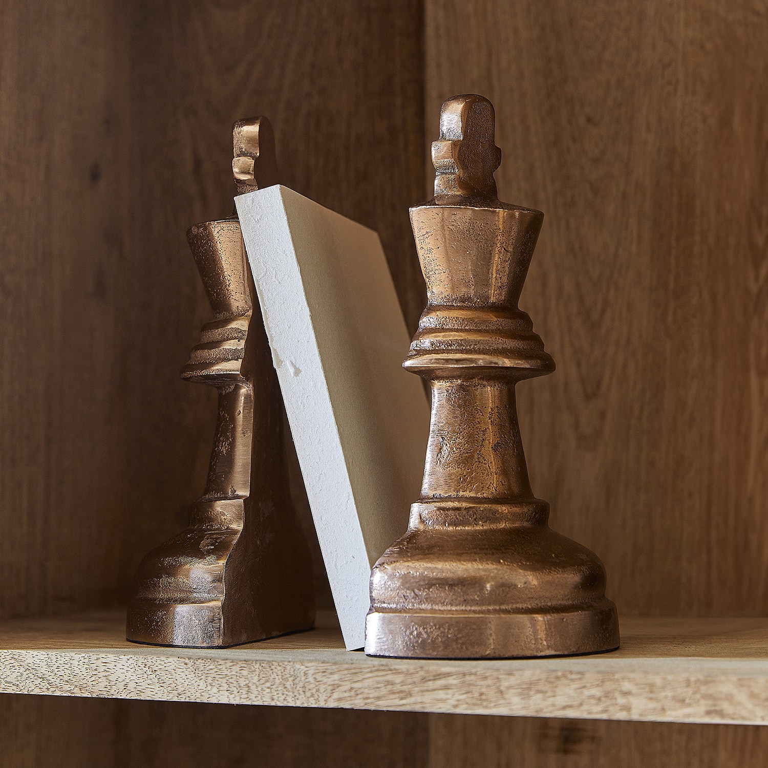 Serre-livres en forme de pièces d'échecs couleur cuivre sur étagère en bois