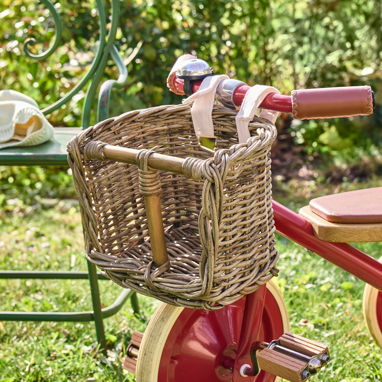 Panier de vélo pour poupée Snokki Panier en osier fixé à un vélo d'enfant rouge avec poignées en cuir, posé sur l'herbe dans un jardin