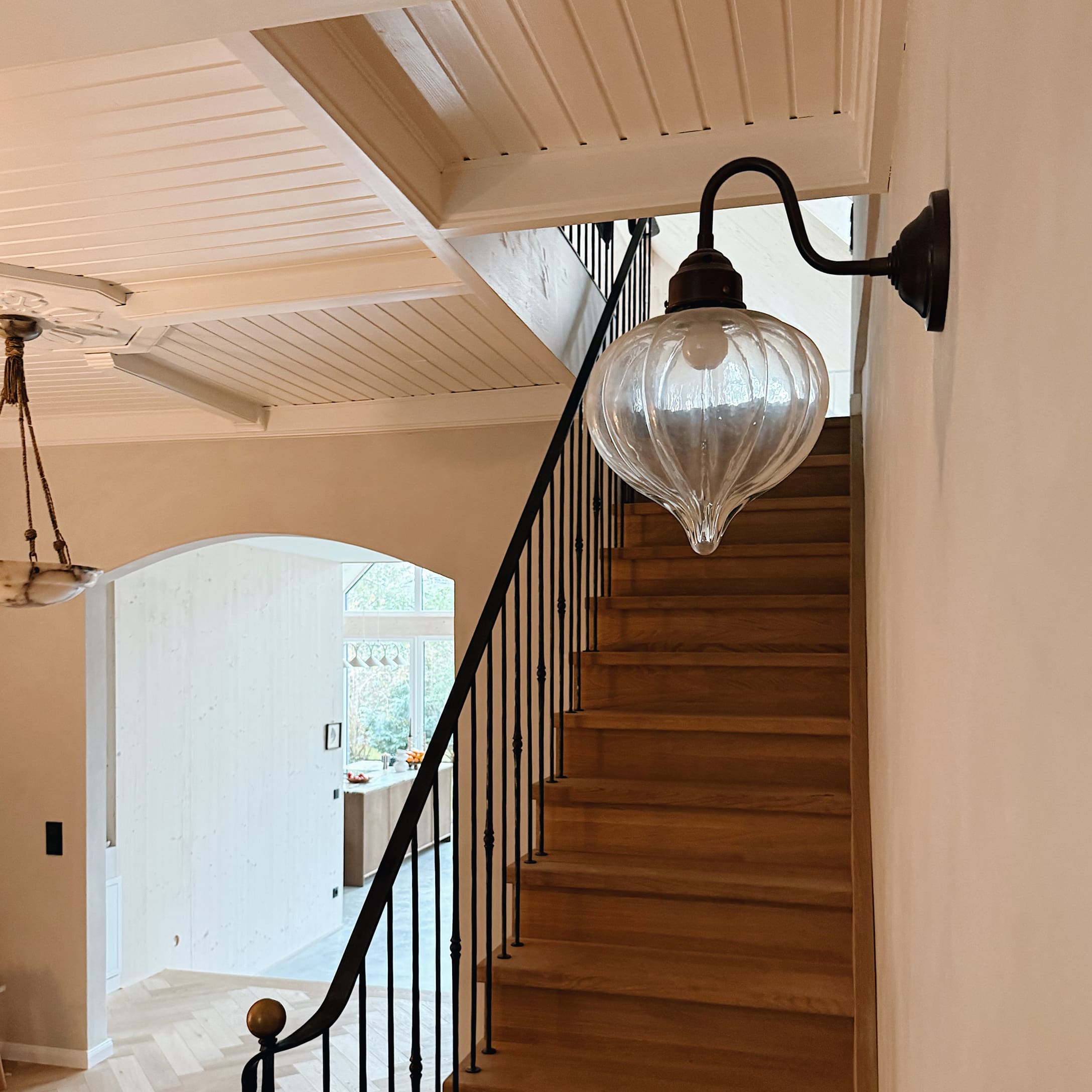 Applique murale en verre avec bras en métal noir au-dessus d'un escalier en bois dans un intérieur clair