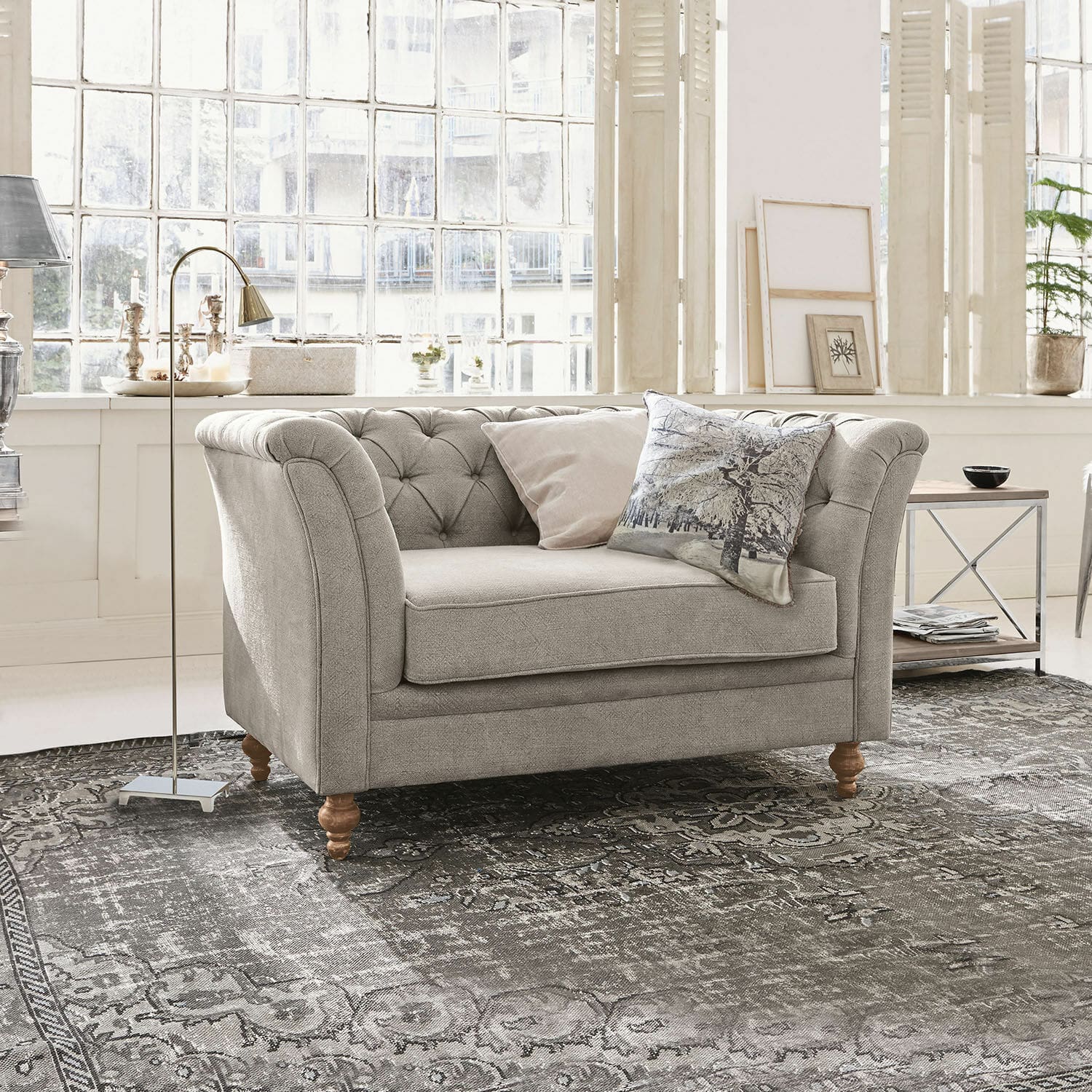 Canapé gris rembourré avec pieds en bois sur tapis à motifs dans un salon lumineux