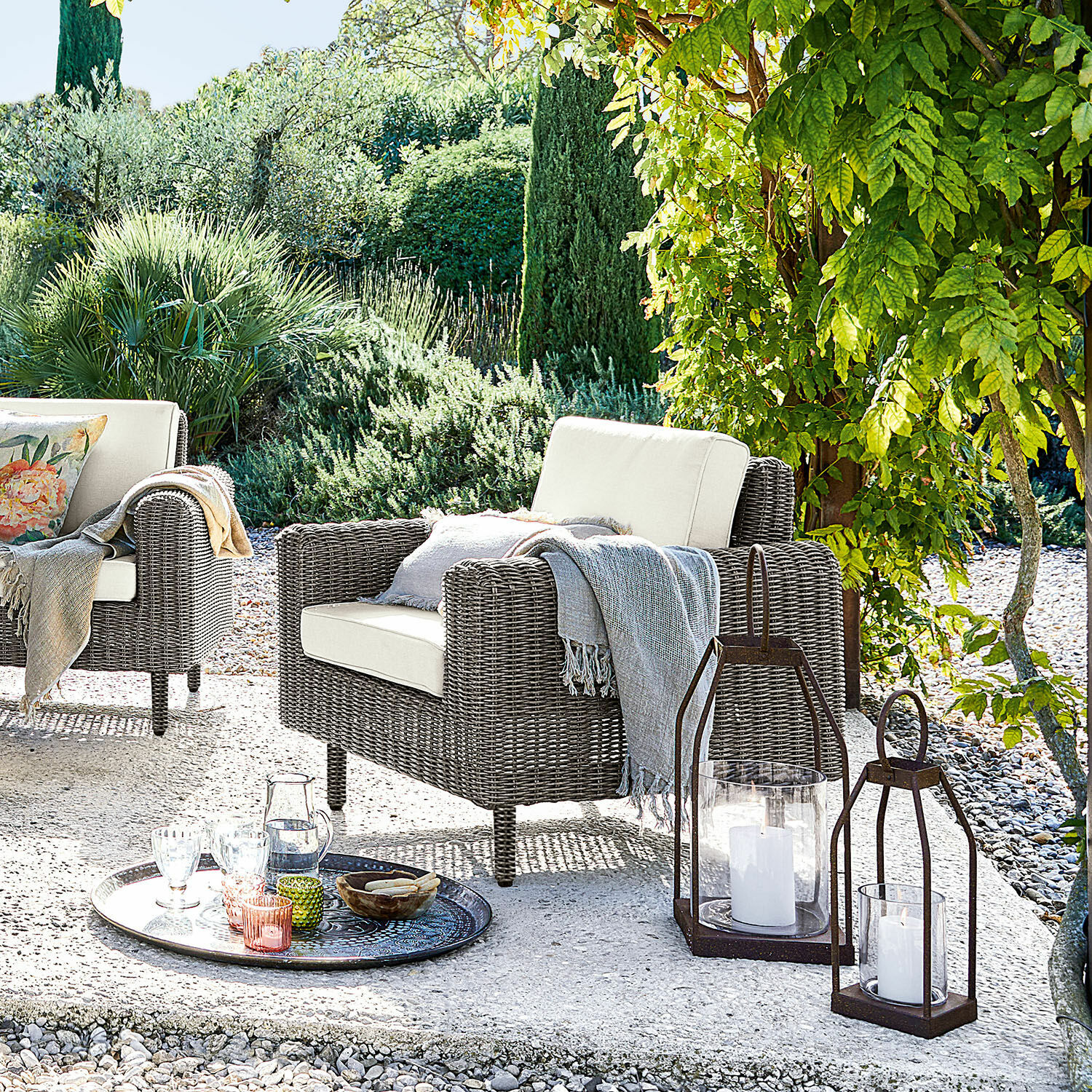 Fauteuil Bardou Fauteuil de jardin en rotin gris avec coussins crème et lanternes décoratives sur la terrasse