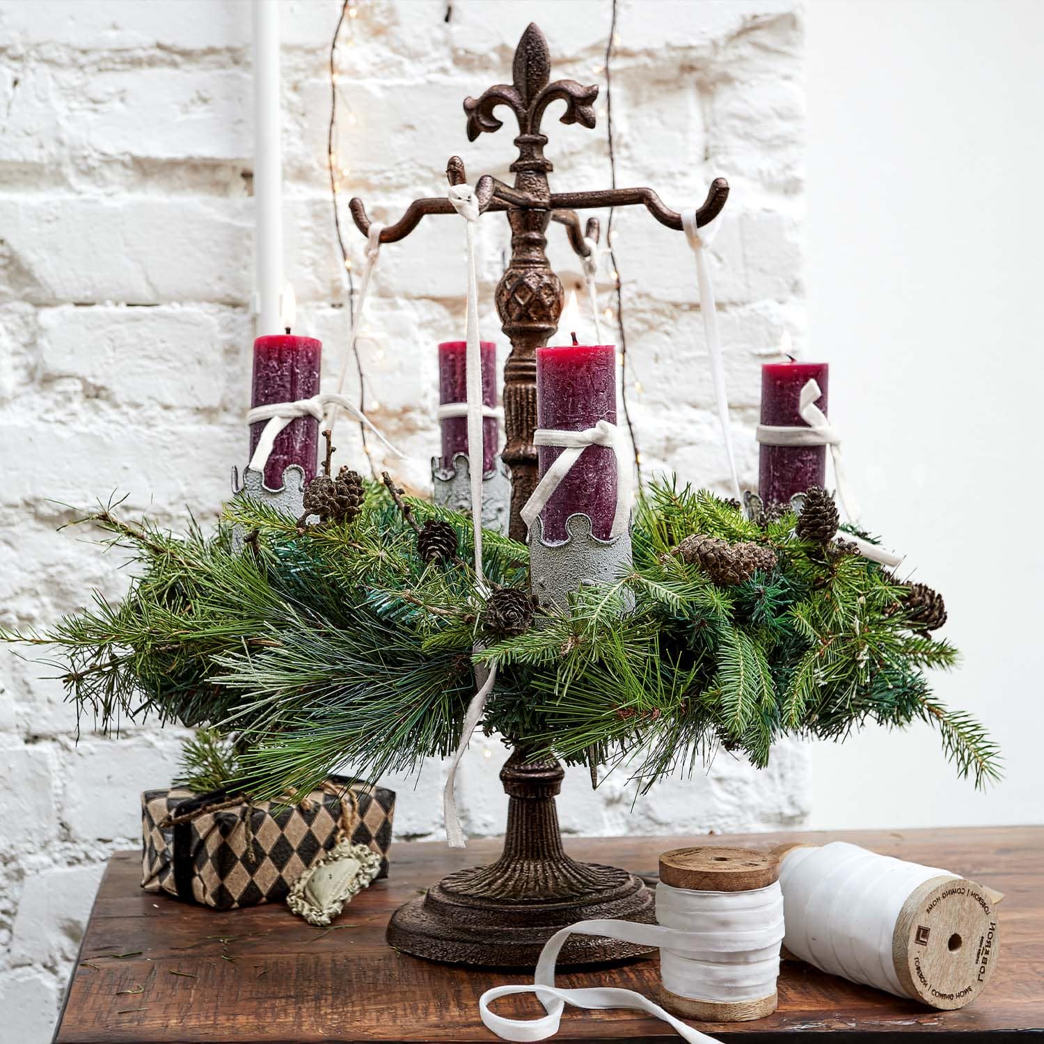 Chandelier en métal avec quatre bougies rouges et branches de sapin vertes sur une table en bois