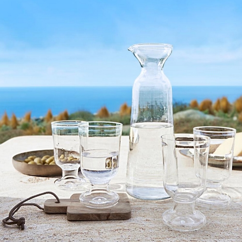 Carafe en verre et quatre verres transparents sur table avec vue sur la mer, verre clair