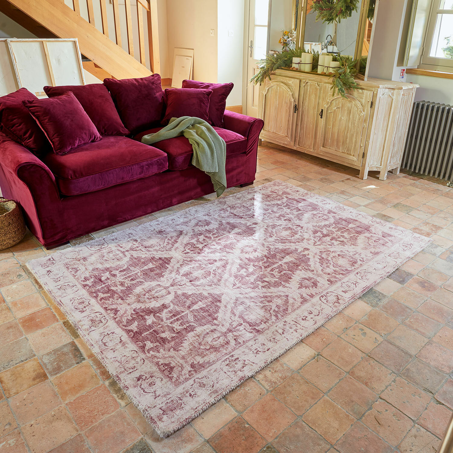 Tapis Mirellis Tapis rose à motif vintage posé devant un canapé en velours bordeaux et un buffet en bois clair