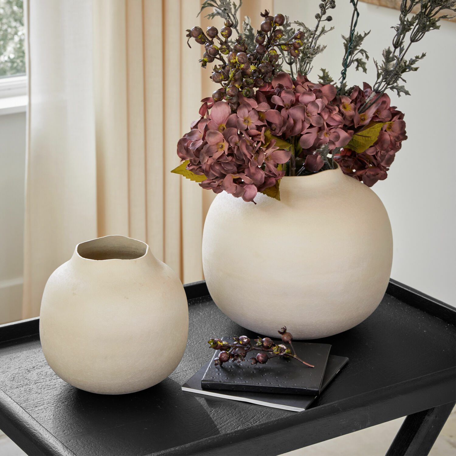 Lot de 2 vases Fleurons Deux vases en céramique crème sur une table noire avec fleurs décoratives et livres en arrière-plan