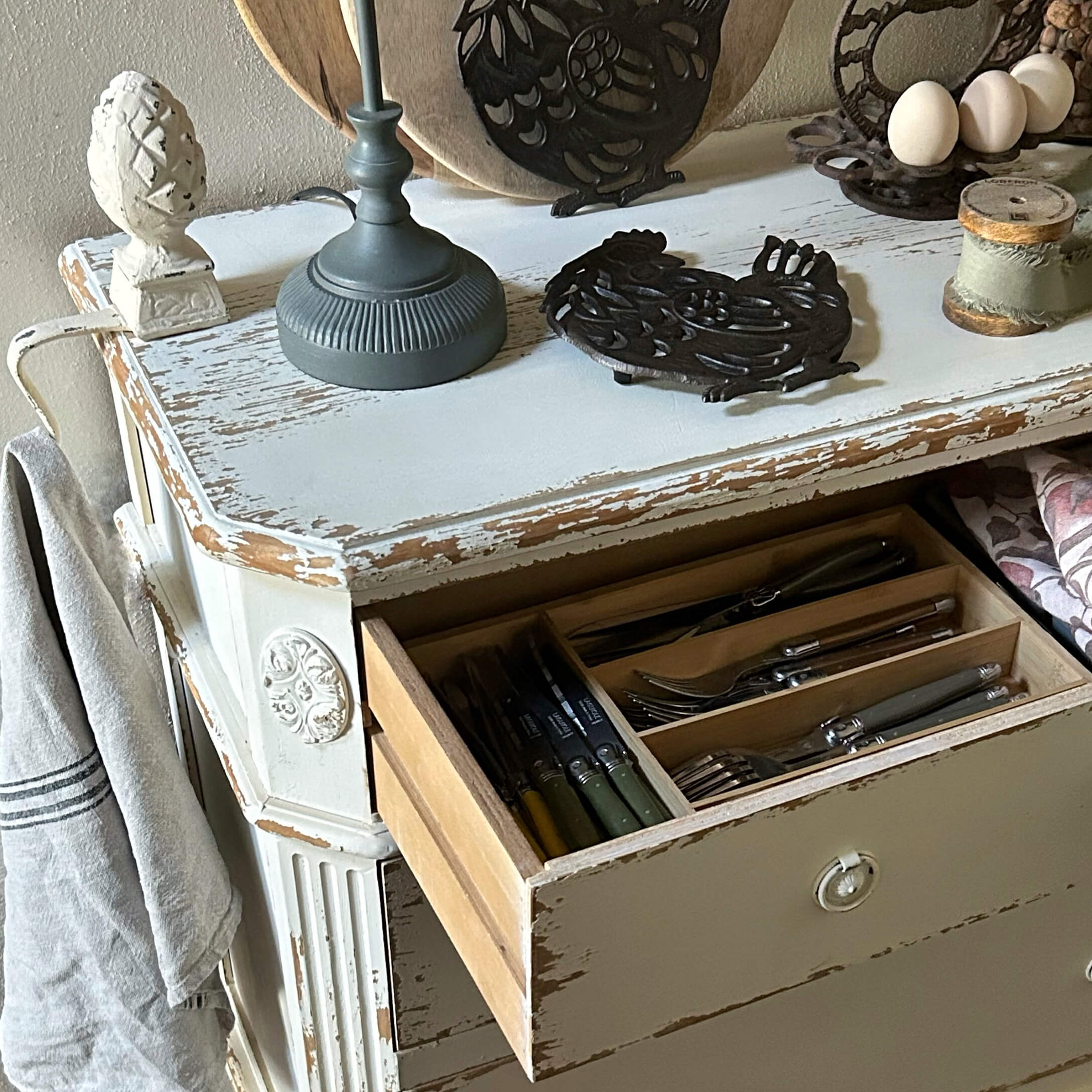 Commode en bois blanc vieilli avec tiroir ouvert contenant des couverts, style rustique pour cuisine