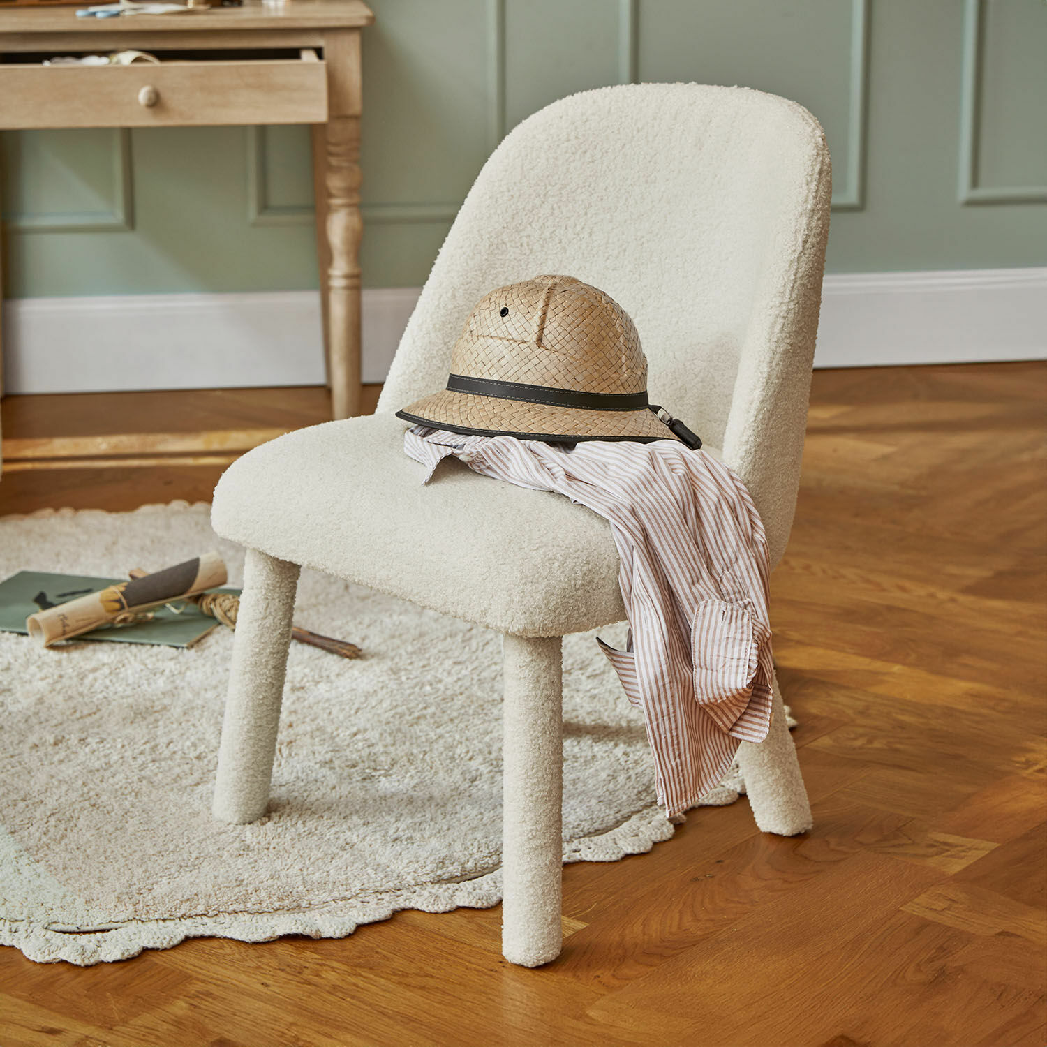 Chaise pour enfant Ivrielle Chaise rembourrée en tissu blanc avec un chapeau en paille et une chemise rayée posés dessus sur un parquet en bois