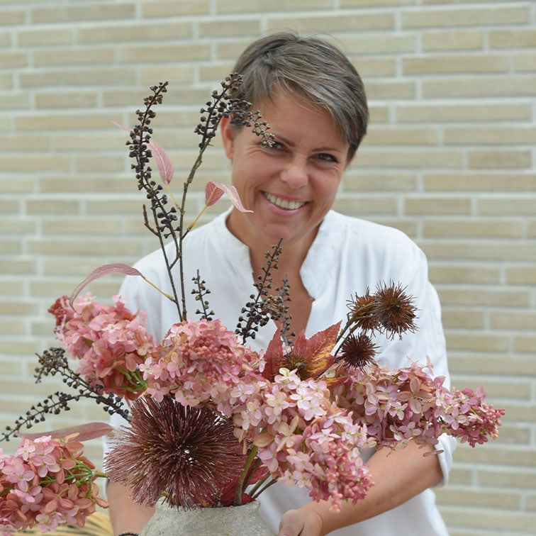 Femme souriante en chemise blanche tenant un vase avec des fleurs séchées roses et brunes décoratives