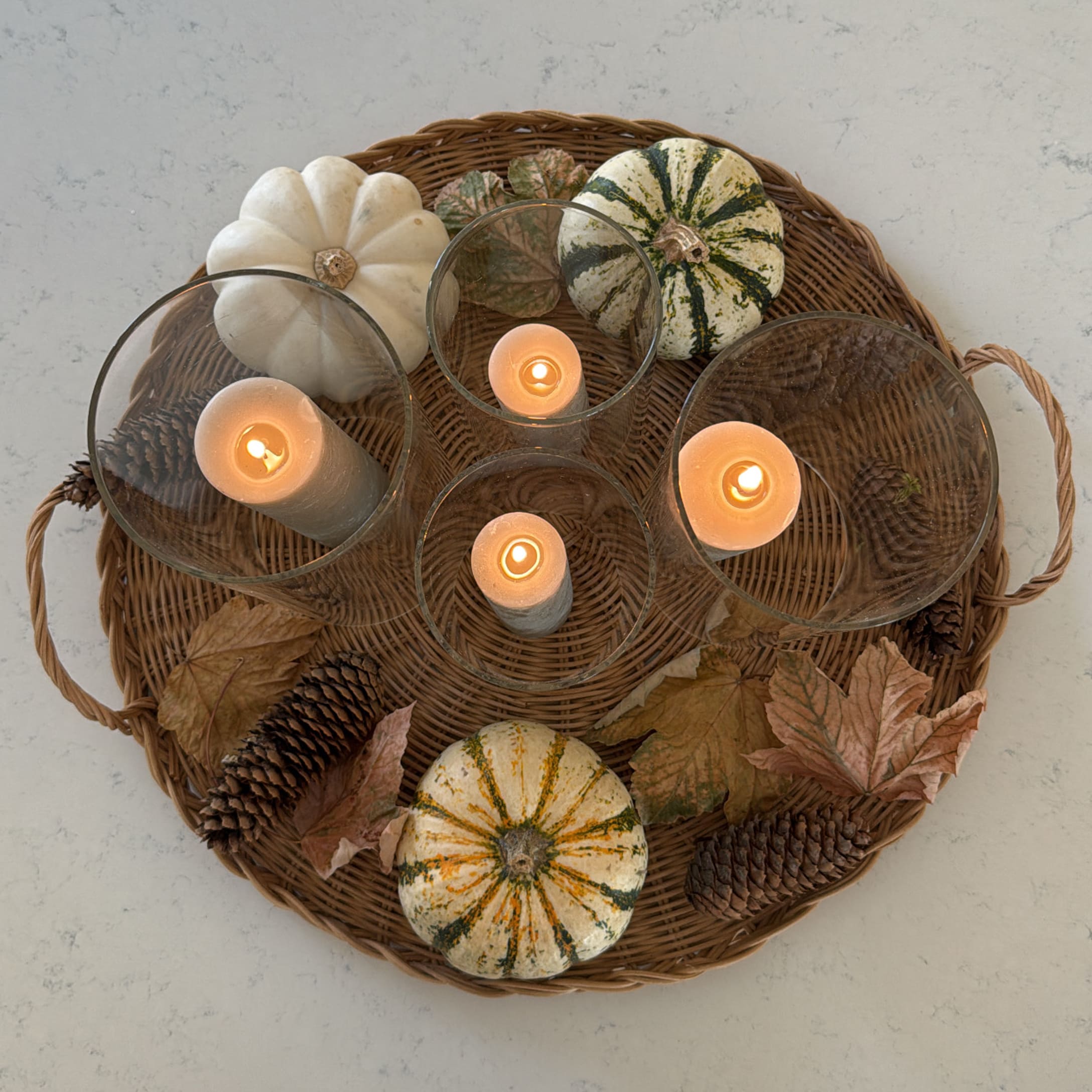 Décoration automnale avec citrouilles blanches et vertes, pommes de pin et bougies sur plateau en osier
