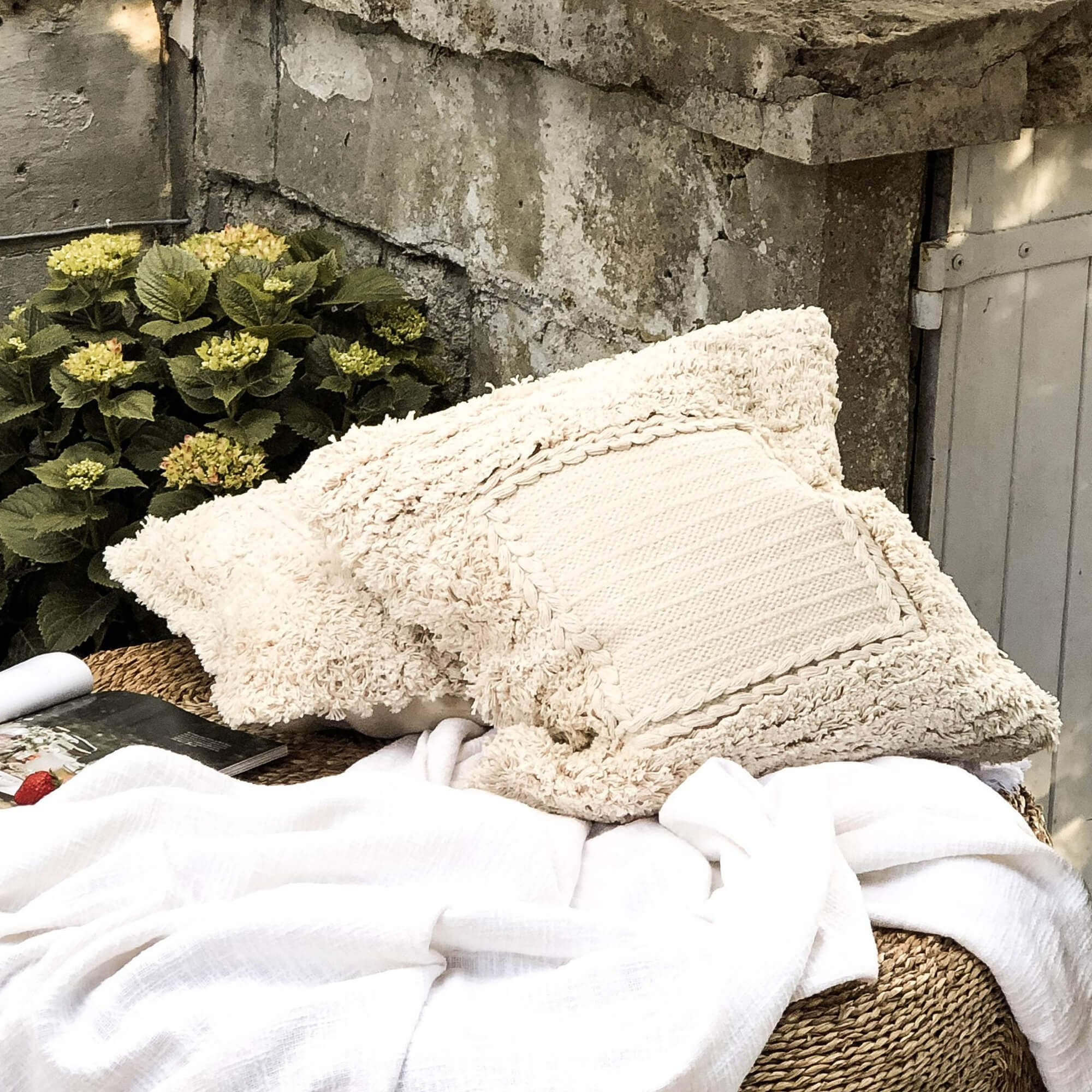 Coussin décoratif beige en tissu doux sur meuble tressé avec couverture blanche en extérieur