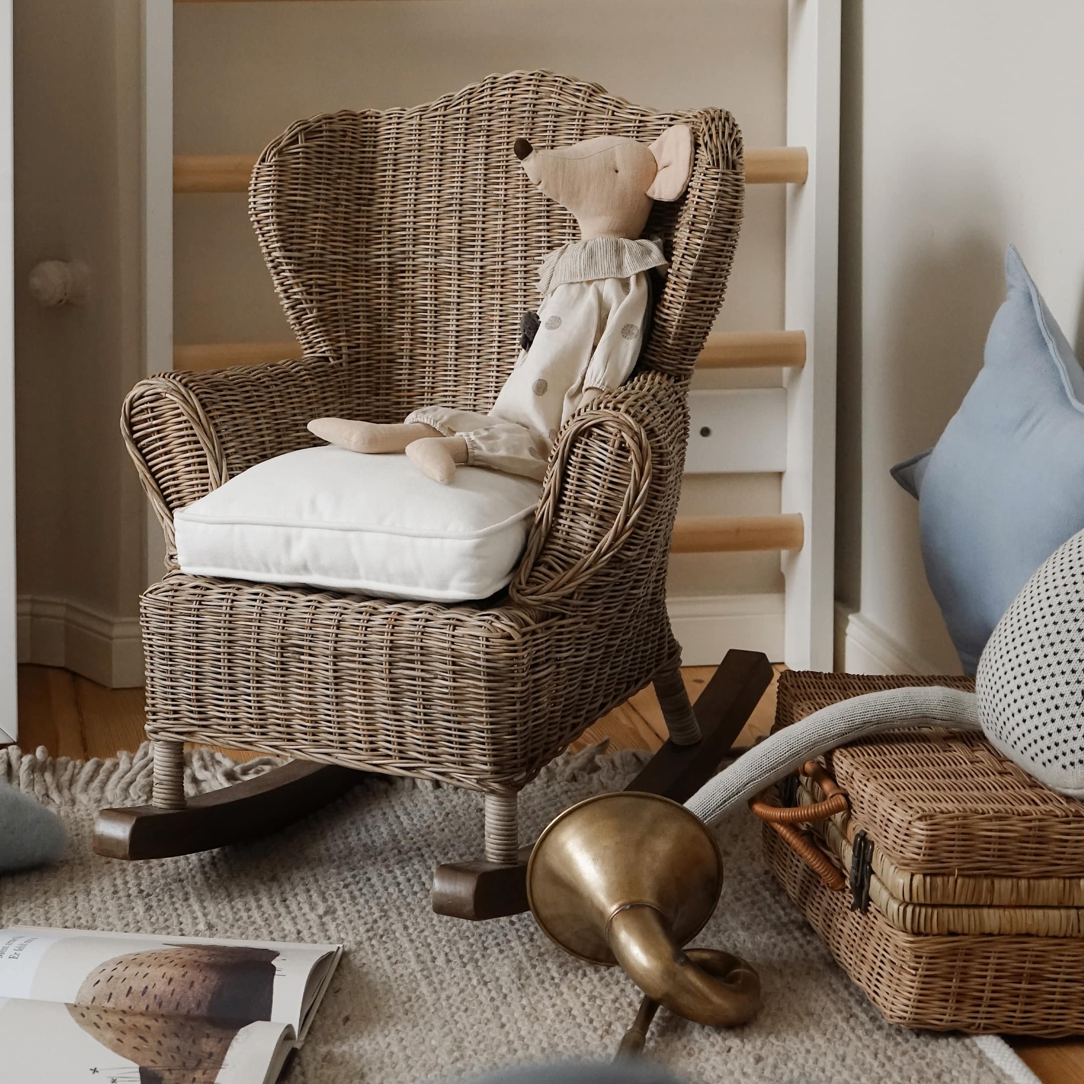 Fauteuil à bascule en rotin avec coussin blanc et souris en peluche dans une chambre d'enfant naturelle