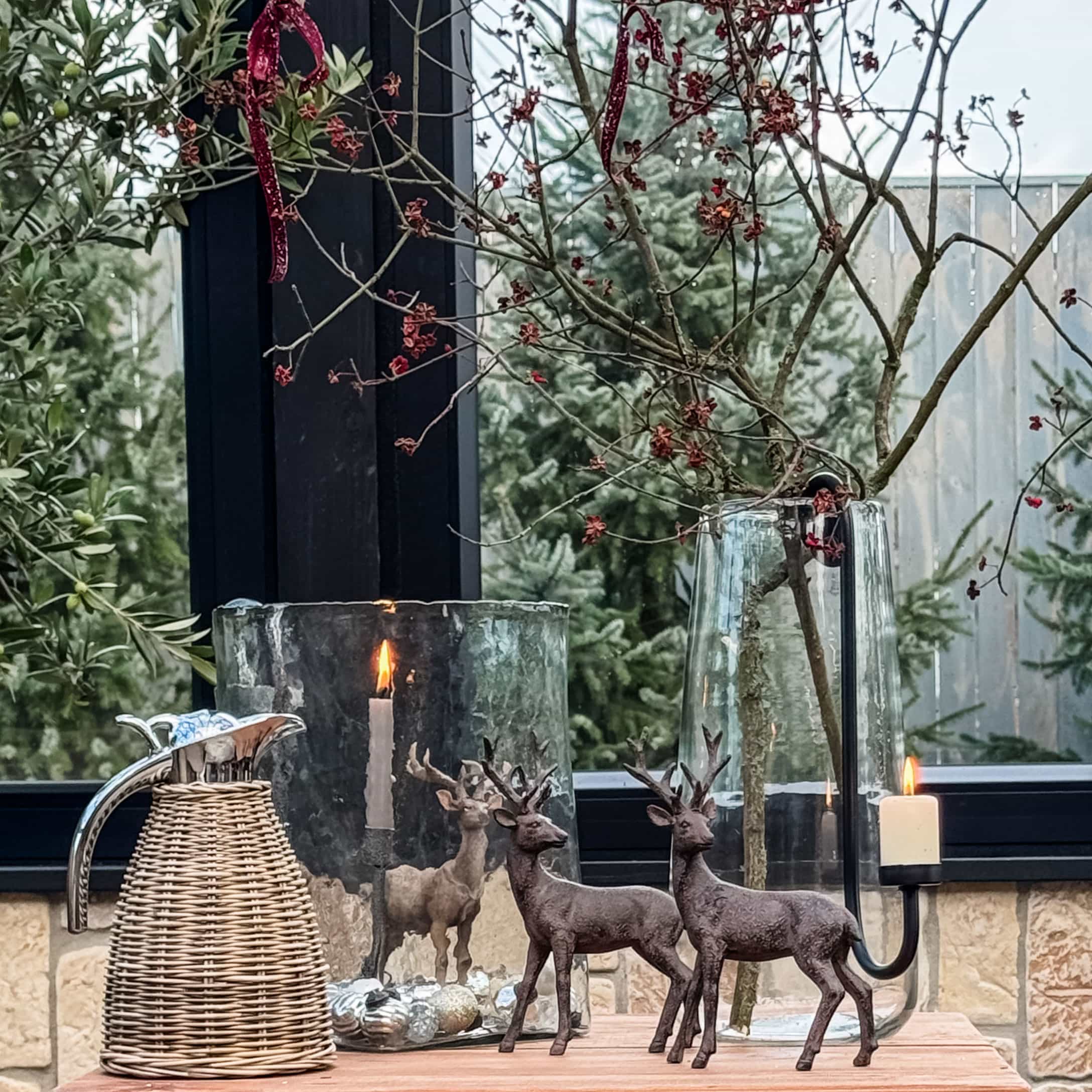 Décoration de Noël avec deux figurines de cerfs bruns, bougie allumée et vase en verre sur table en bois
