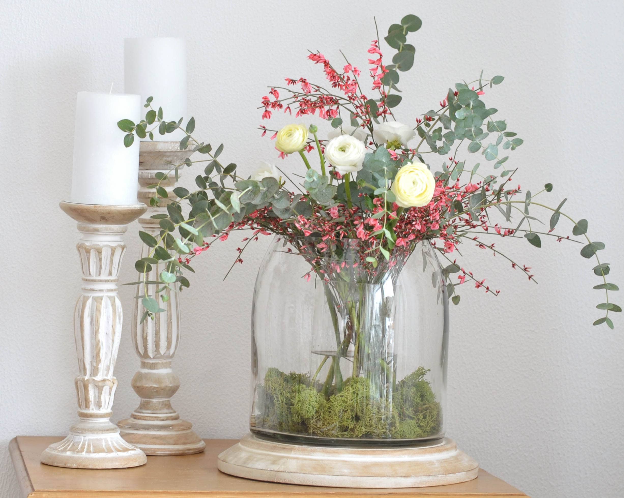Bouquet décoratif de fleurs blanches et roses dans un vase en verre sur socle en bois avec bougies blanches