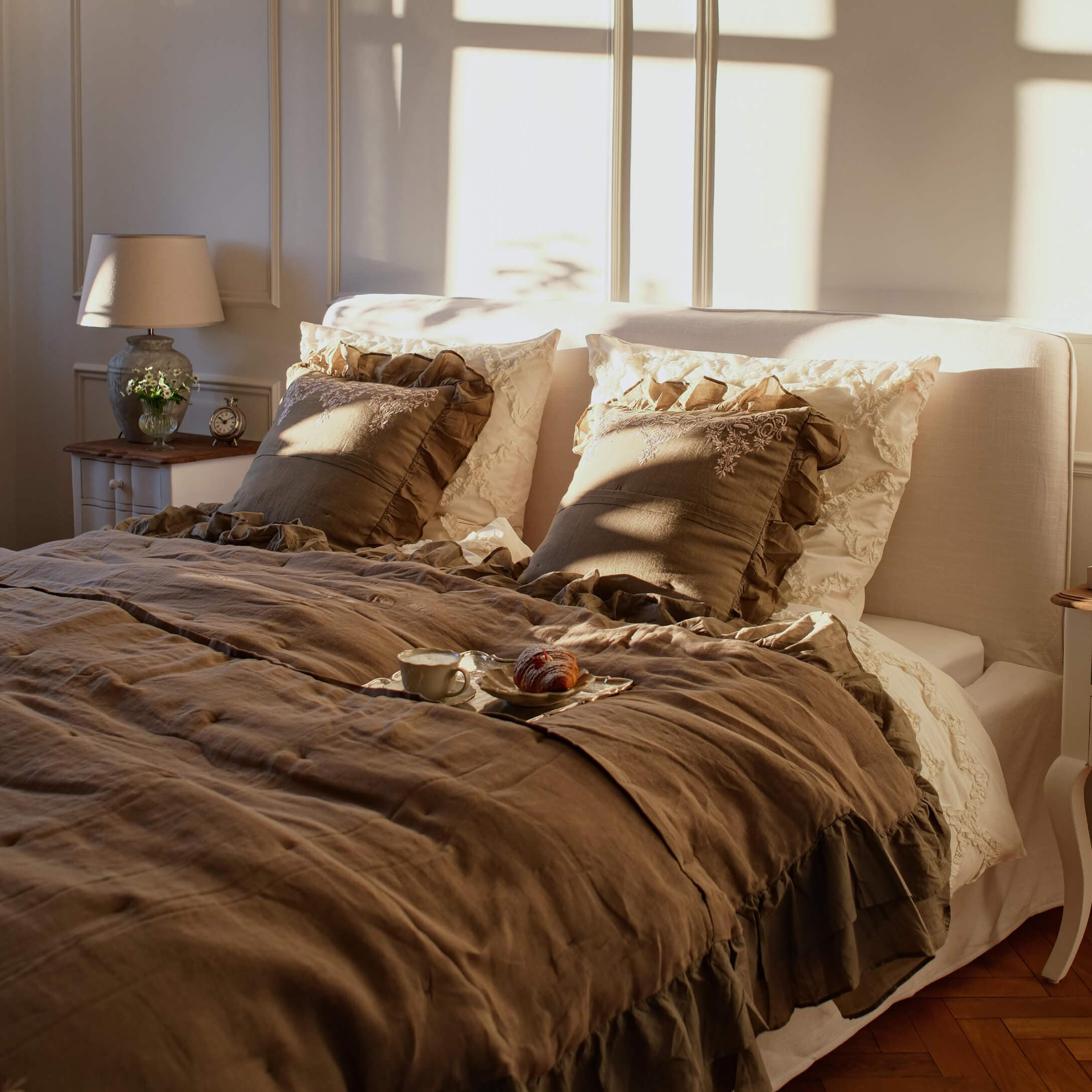 Chambre chaleureuse avec linge de lit en lin beige et coussins à volants marron dans une lumière douce