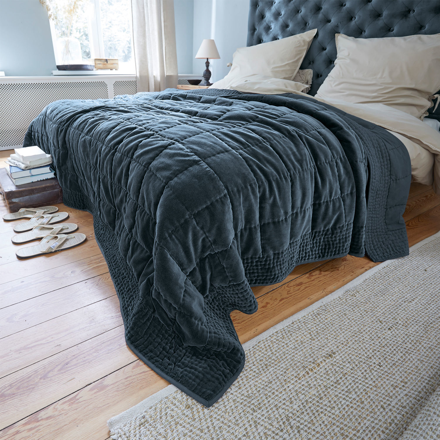 Courtepointe Arasta Plaid matelassé bleu marine en tissu doux sur un lit dans une chambre claire avec parquet en bois